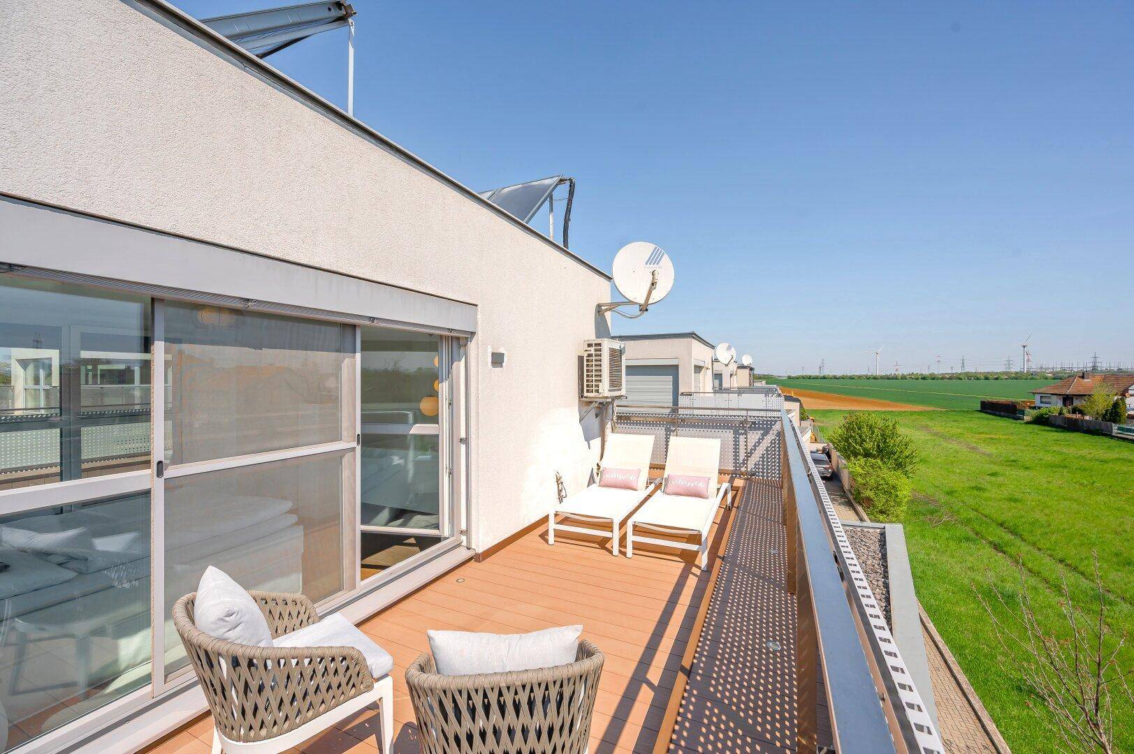 Langer Balkon mit Liegestühlen und weitem Blick über die grüne Landschaft.
