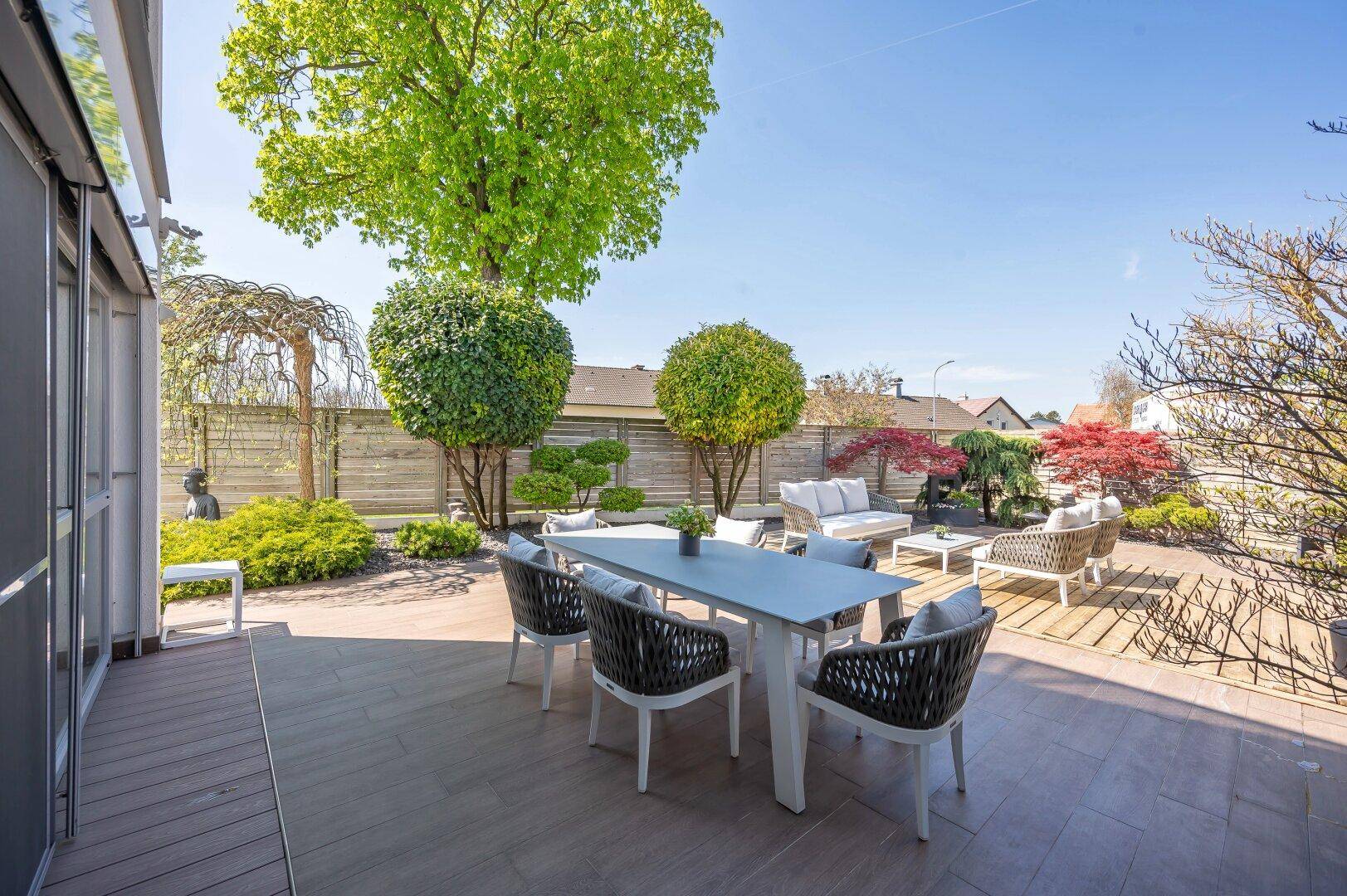 Große Terrasse mit Esstisch und Stühlen, umgeben von gepflegter Gartenlandschaft.