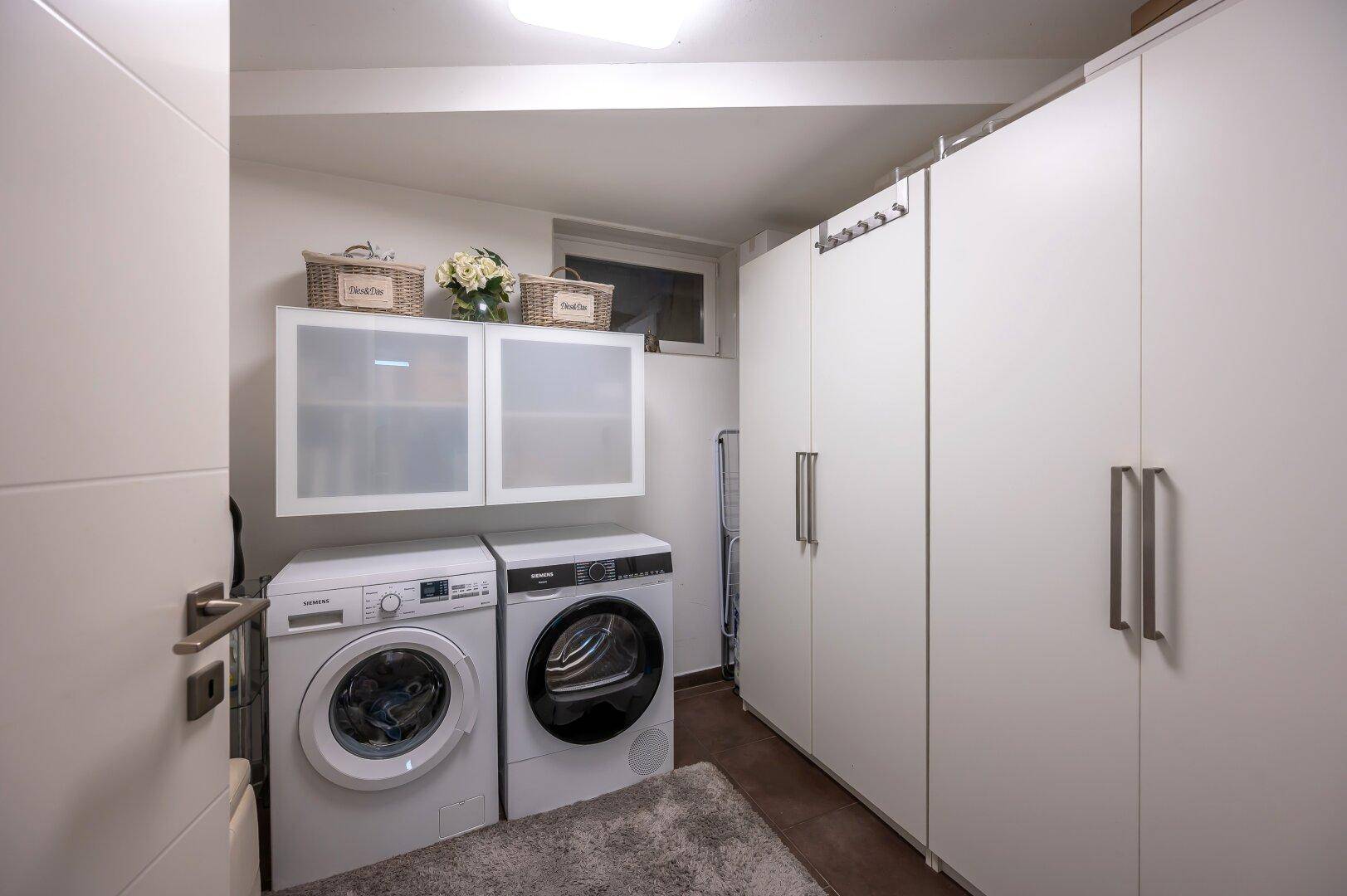Heller Hauswirtschaftsraum mit Waschmaschine, Trockner und praktischen Schränken.