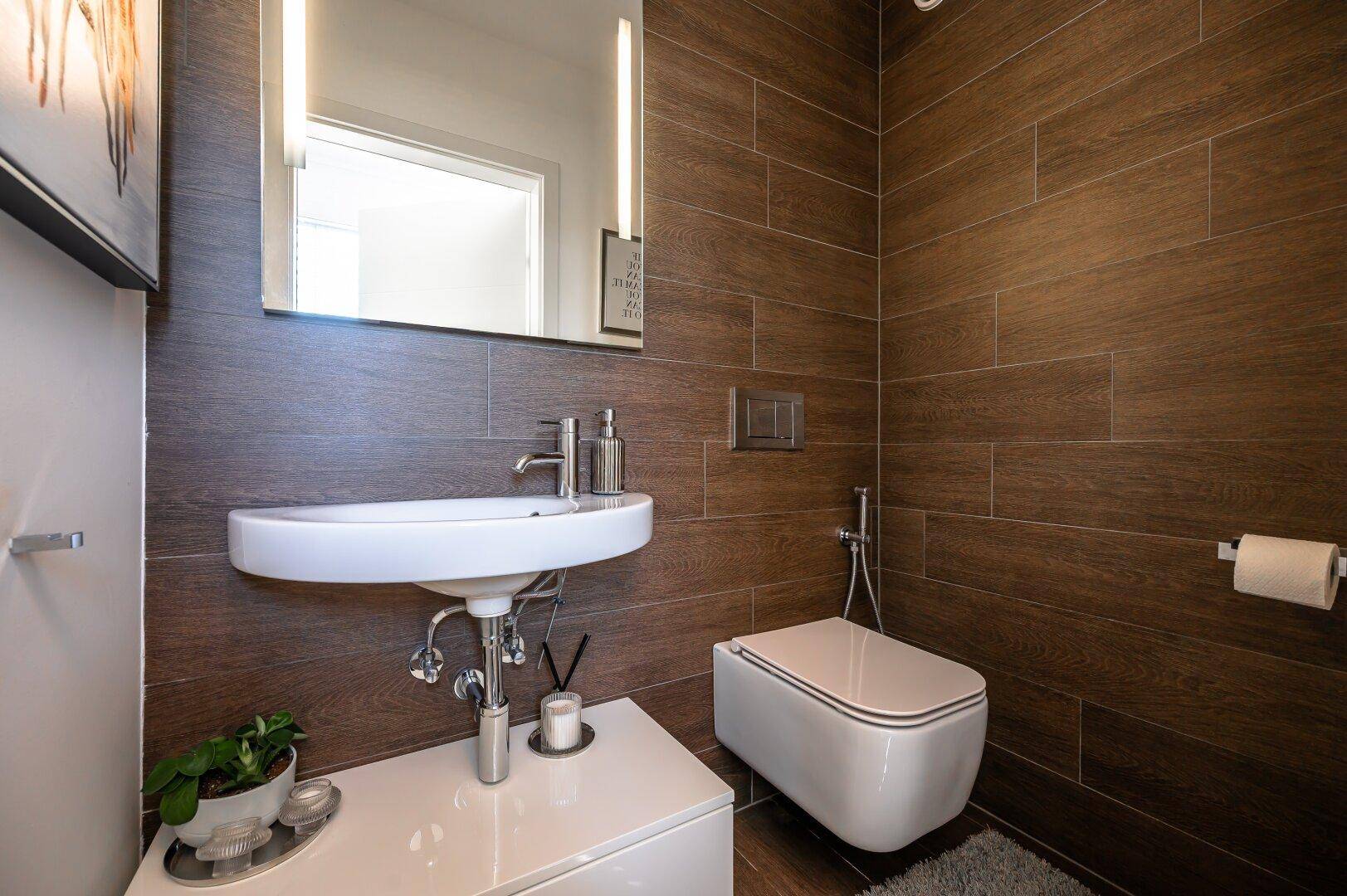 Modernes Gäste-WC mit Holzoptik-Fliesen, wandhängendem WC und kleinem Waschbecken.