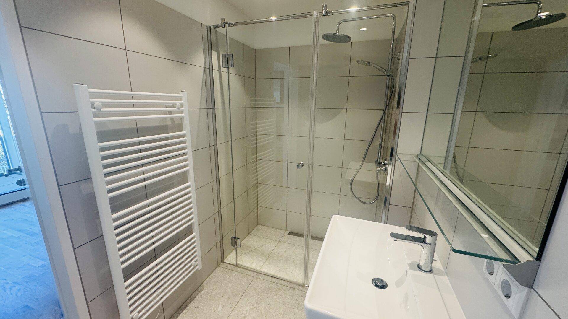 Modernes Badezimmer mit ebenerdiger Dusche, Handtuchheizkörper und hellen Fliesen.