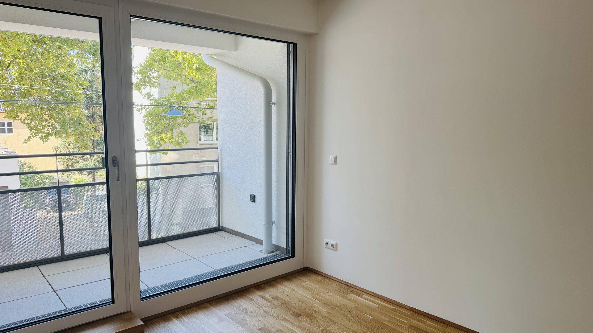 Schlafzimmer mit hellem Parkettboden und Zugang zu einem privaten Balkon.