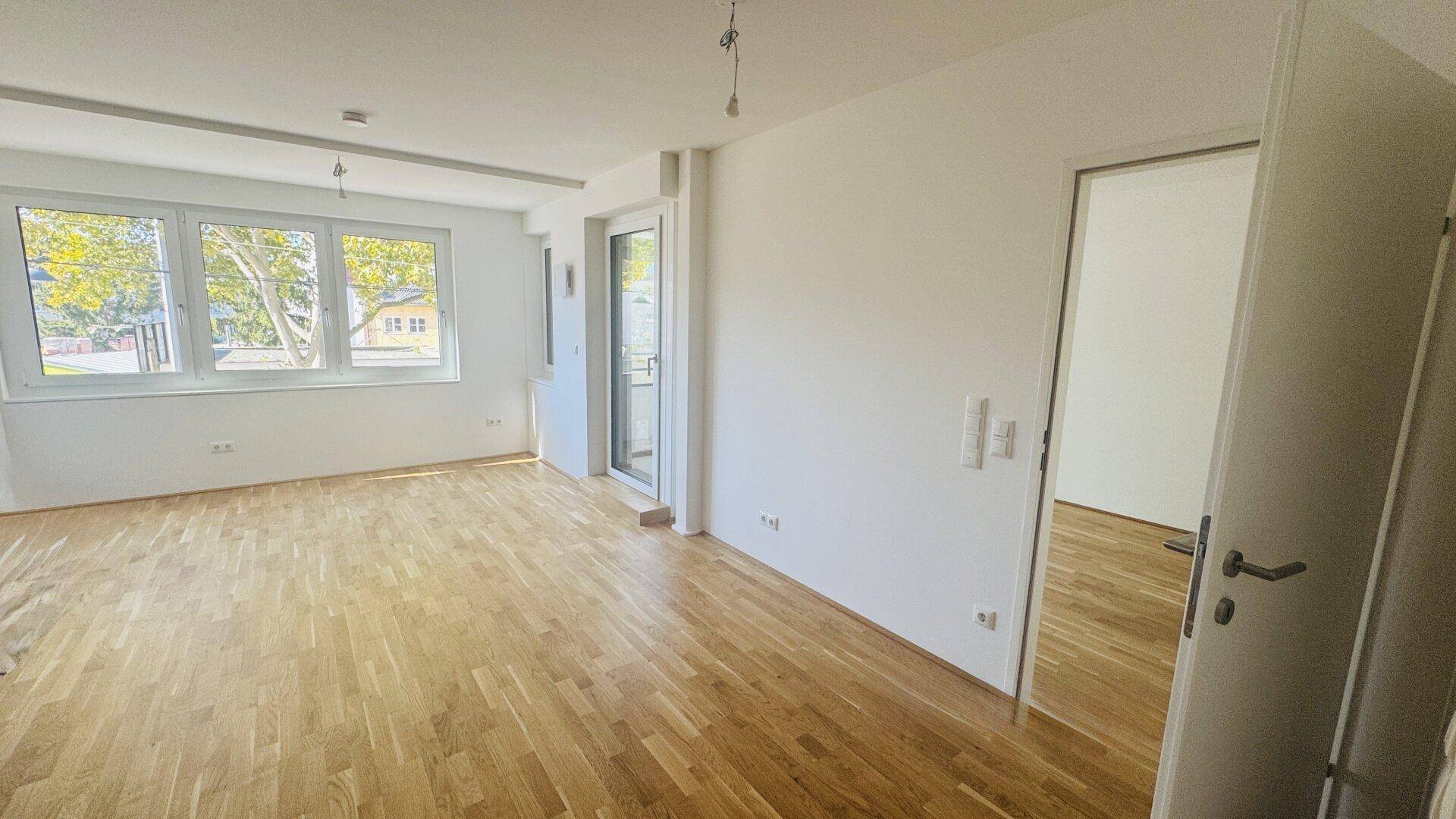 Geräumiger Wohnbereich mit hellem Parkettboden und viel Tageslicht durch große Fenster.