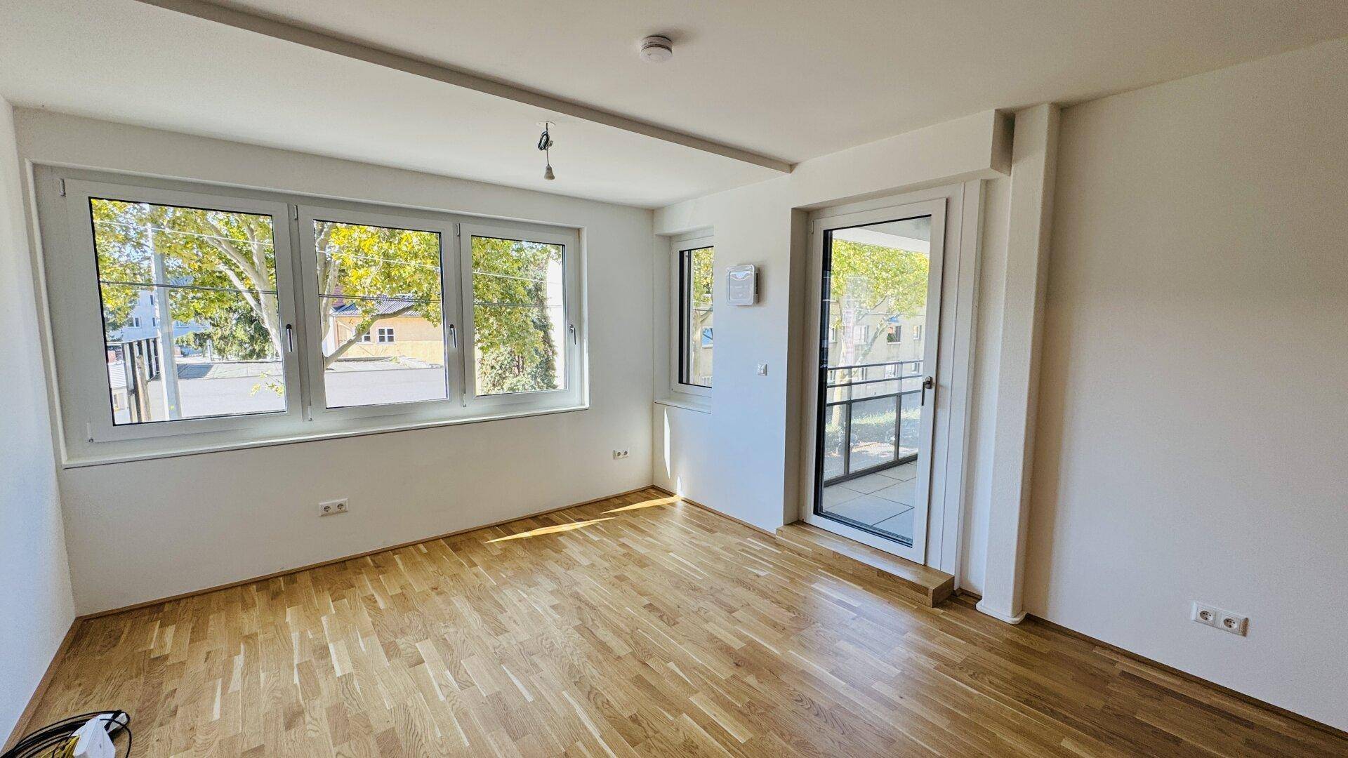 Heller Wohnraum mit Parkettboden, großen Fenstern und Zugang zu einem Balkon.