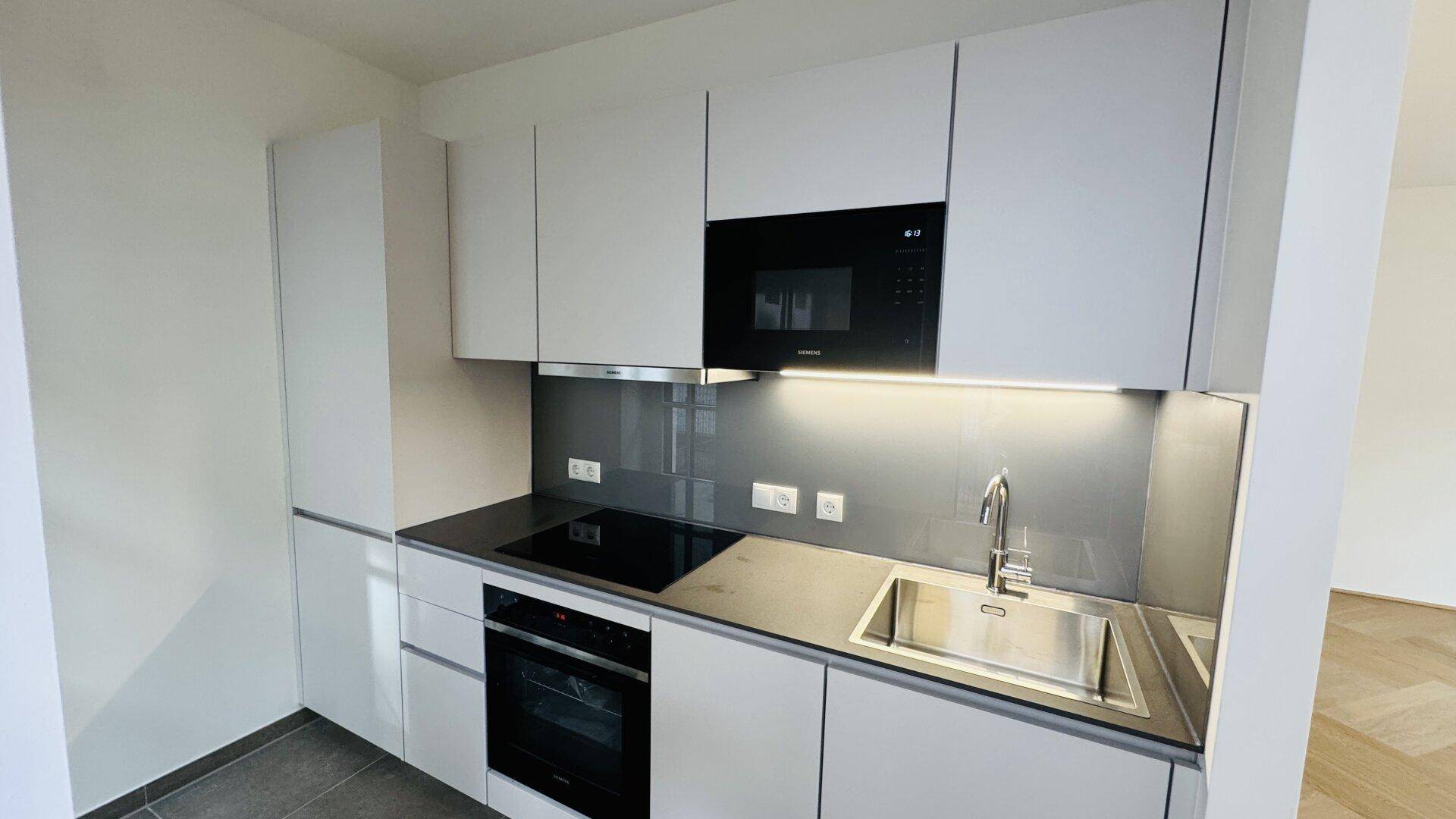 Moderne Einbauküche mit hellgrauen Fronten, Induktionskochfeld und integriertem Backofen.