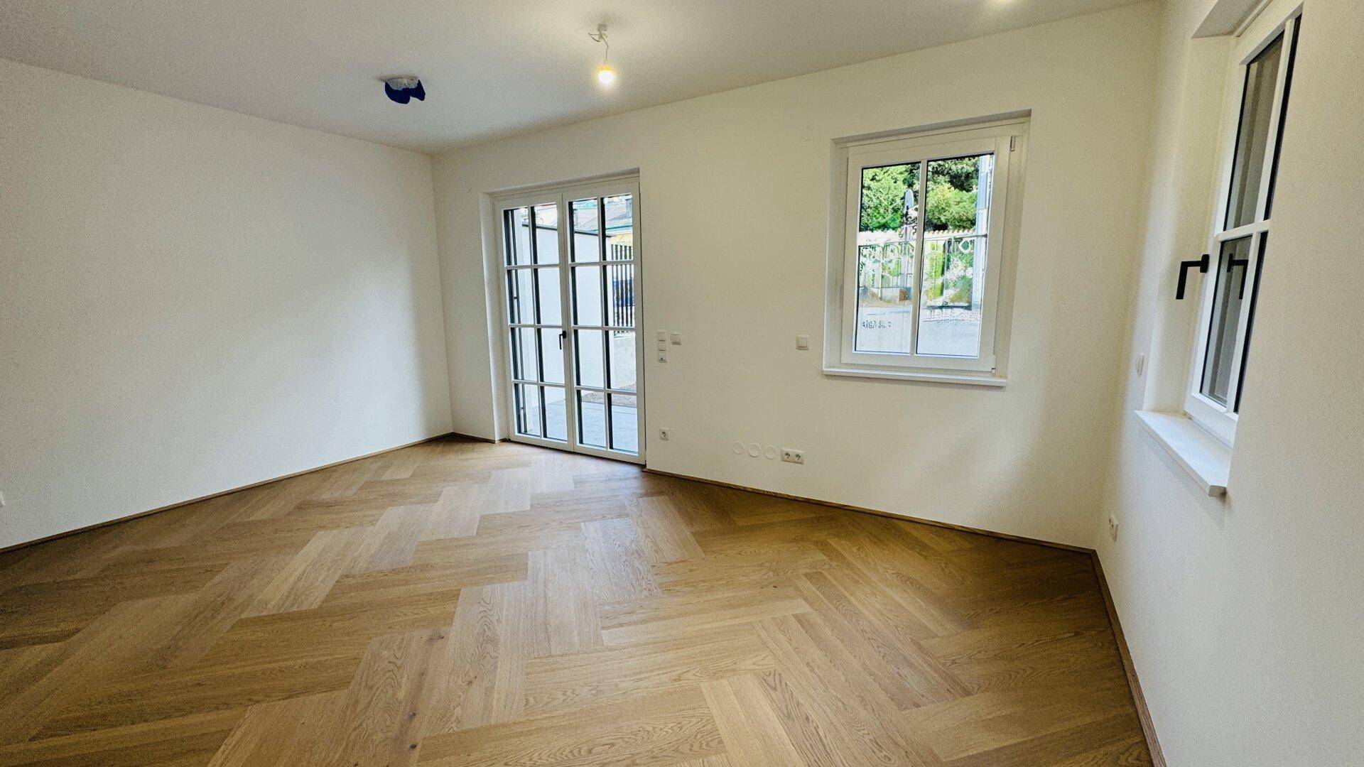 Helles, leeres Zimmer mit Fischgrätparkett und Zugang zu einem Außenbereich.