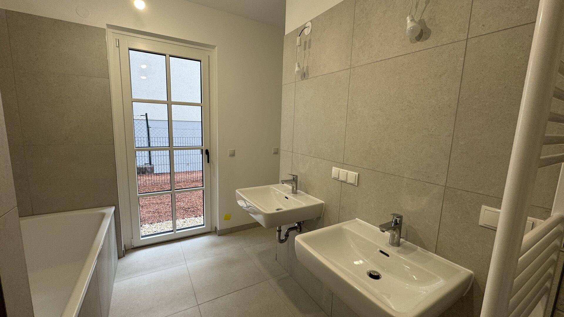 Modernes Badezimmer mit Doppelwaschbecken, Badewanne und Zugang zum Außenbereich.