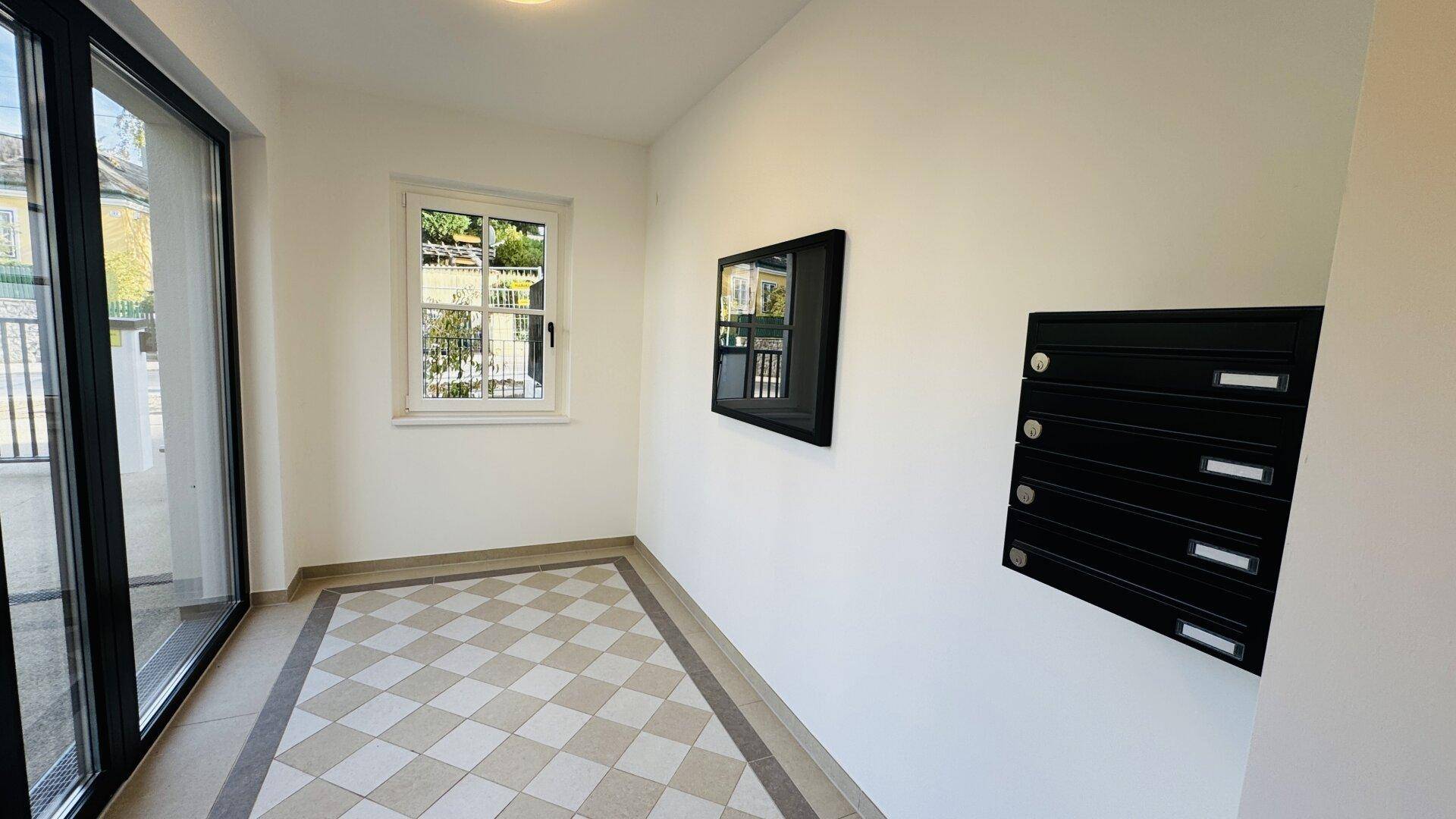 Eingangsbereich mit kariertem Fliesenboden, Fenster und Briefkästen.