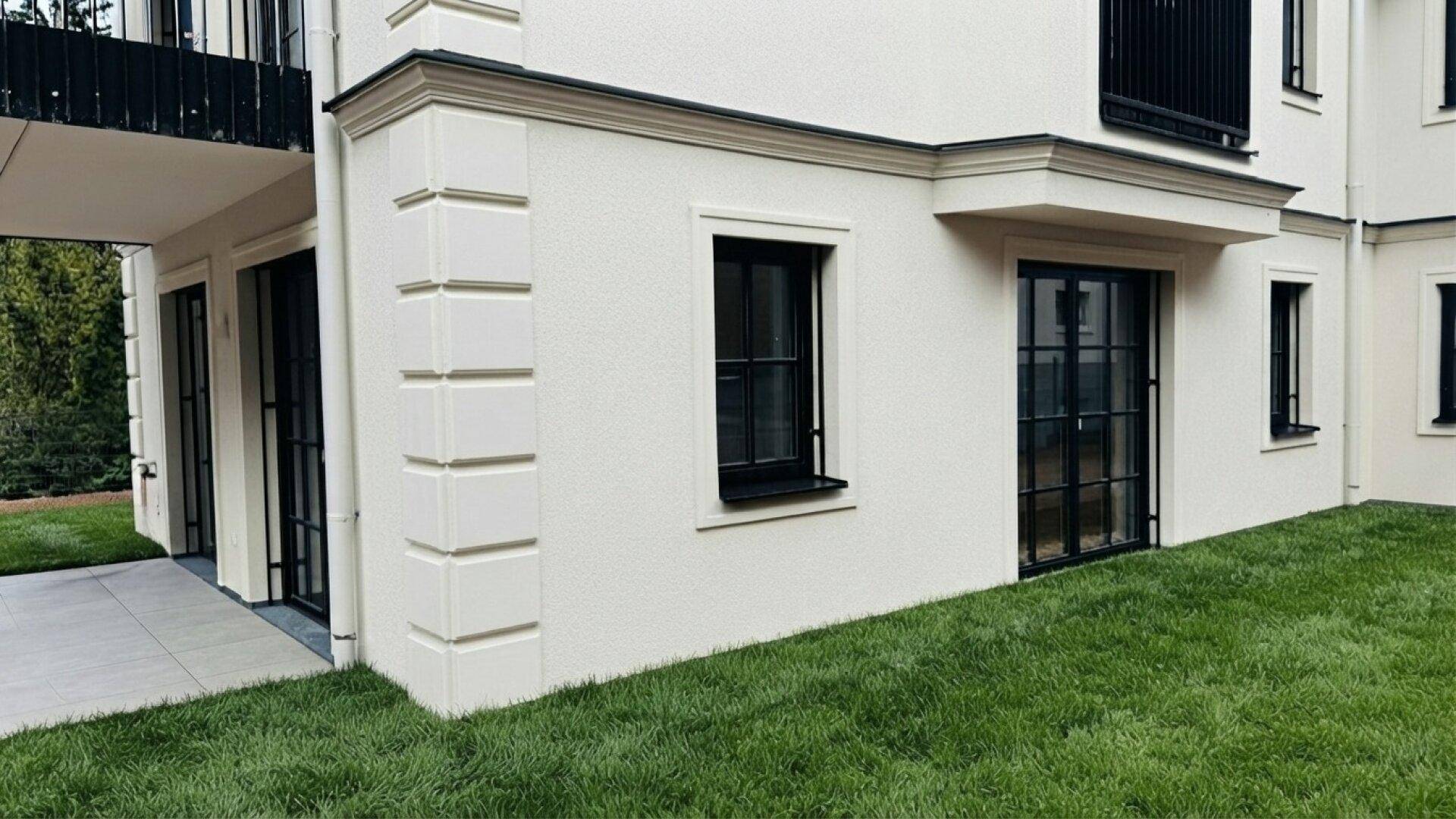 Gebäudefassade mit klassischer Architektur, kleinen Fenstern und angrenzender Rasenfläche.