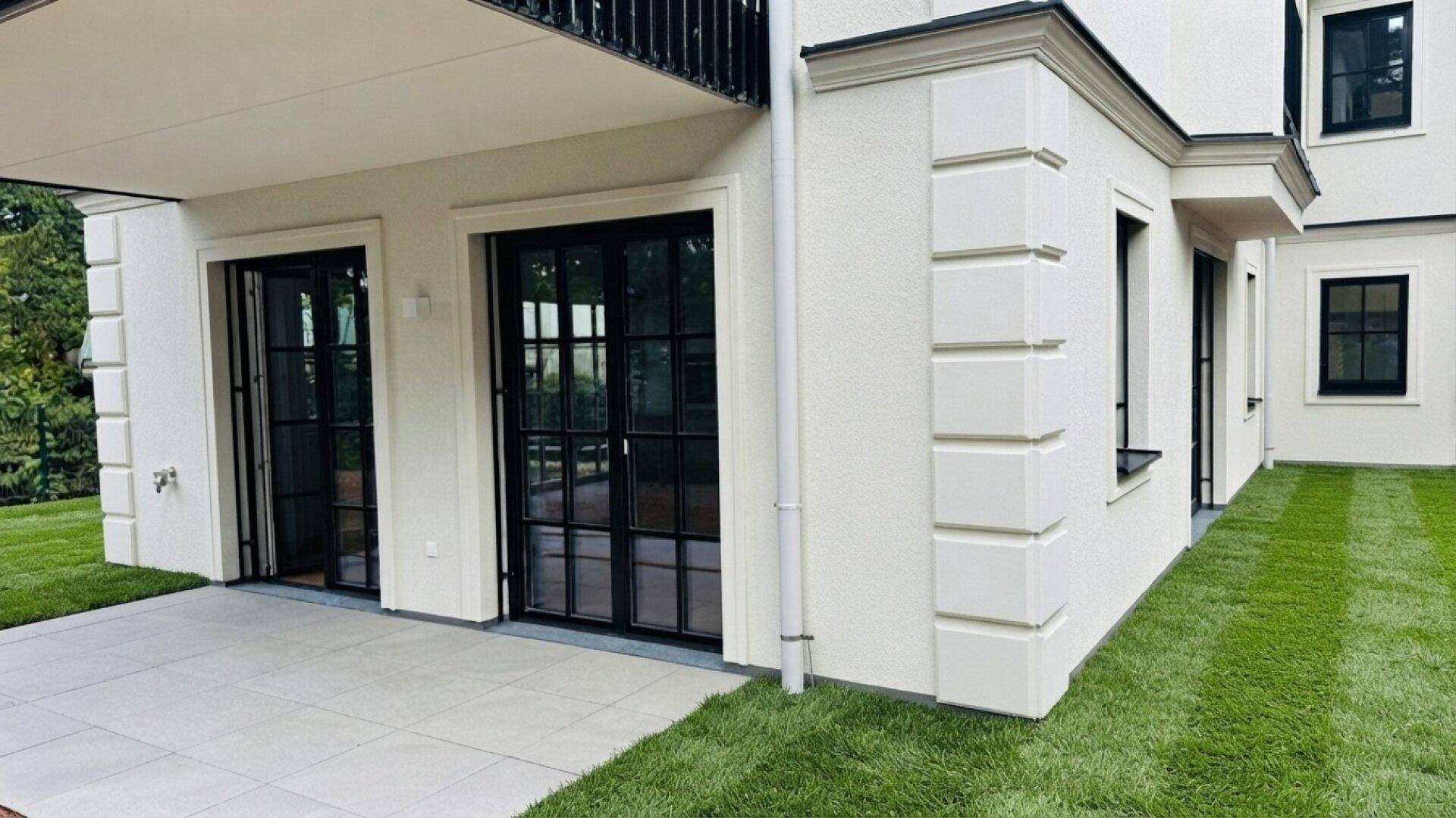 Gebäudefassade mit Terrasse und gepflegter Rasenfläche, ideal für entspannte Stunden im Freien.