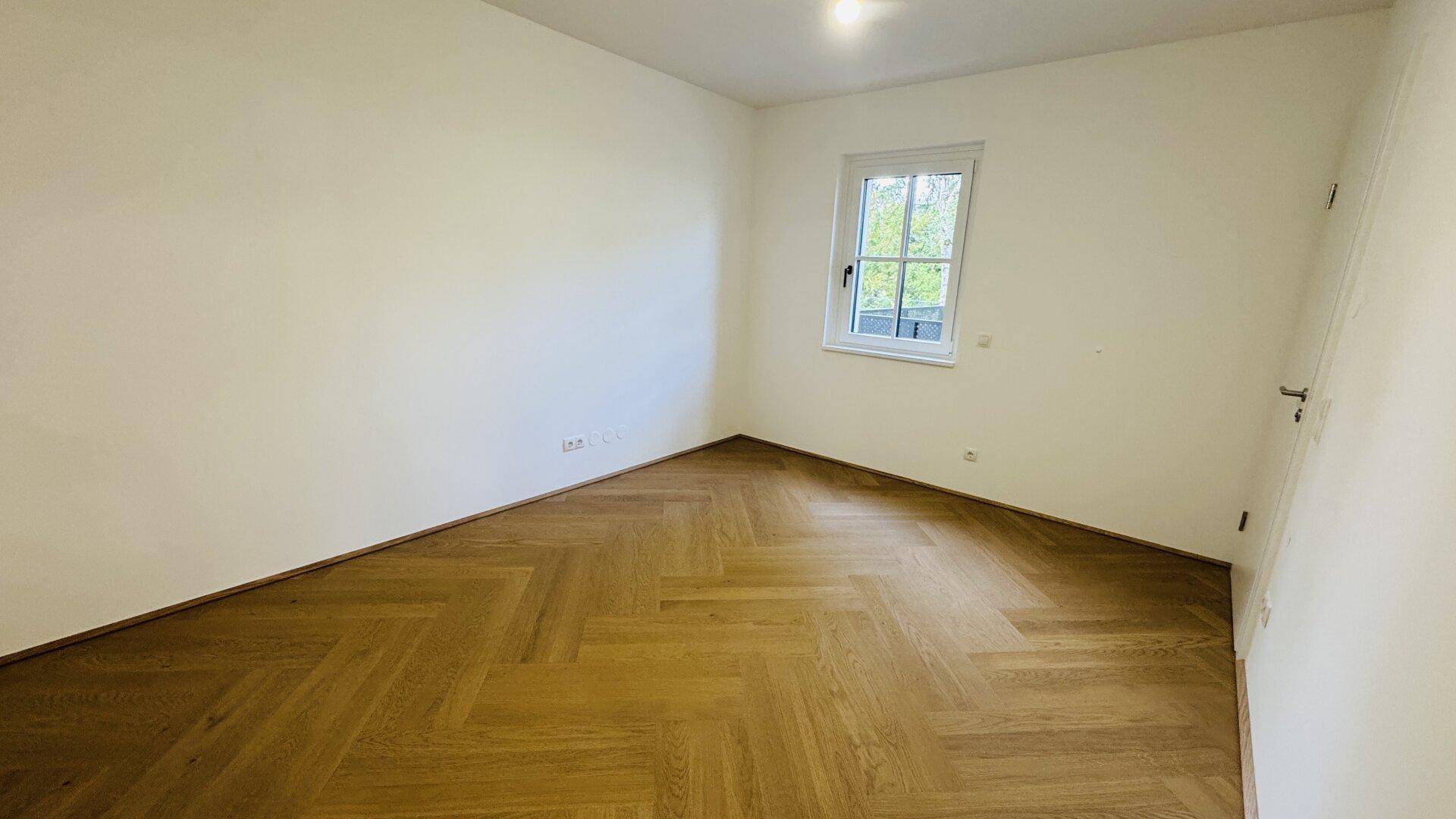Leeres Zimmer mit Fischgrätparkett und einem Fenster, bereit zur individuellen Gestaltung.