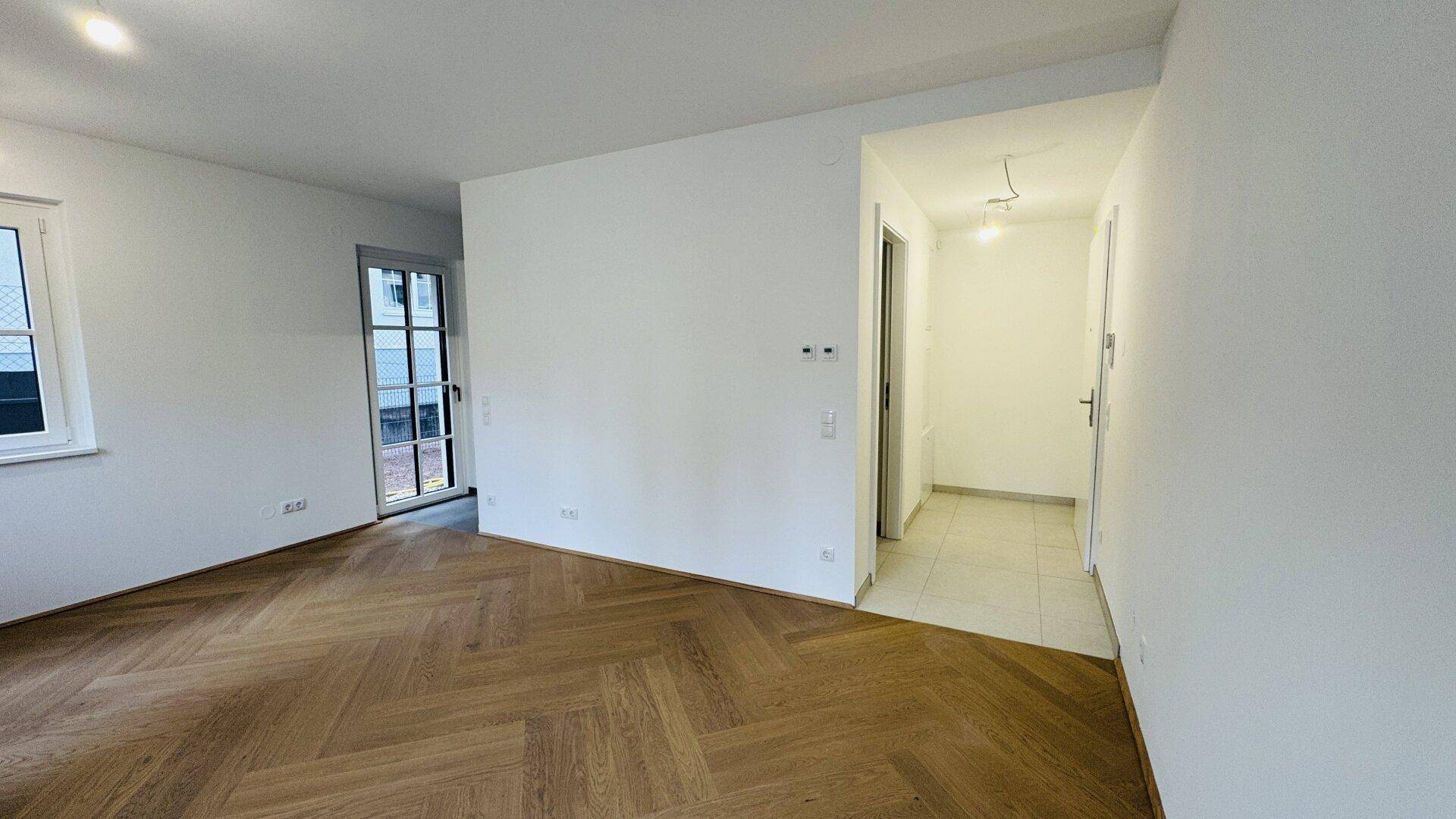 Geräumiges Wohnzimmer mit Fischgrätparkett und Blick auf den Eingangsbereich.