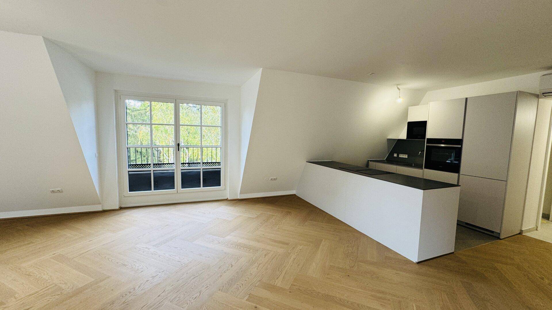 Offener Wohnbereich mit moderner Küche, Parkettboden und Zugang zum Balkon.