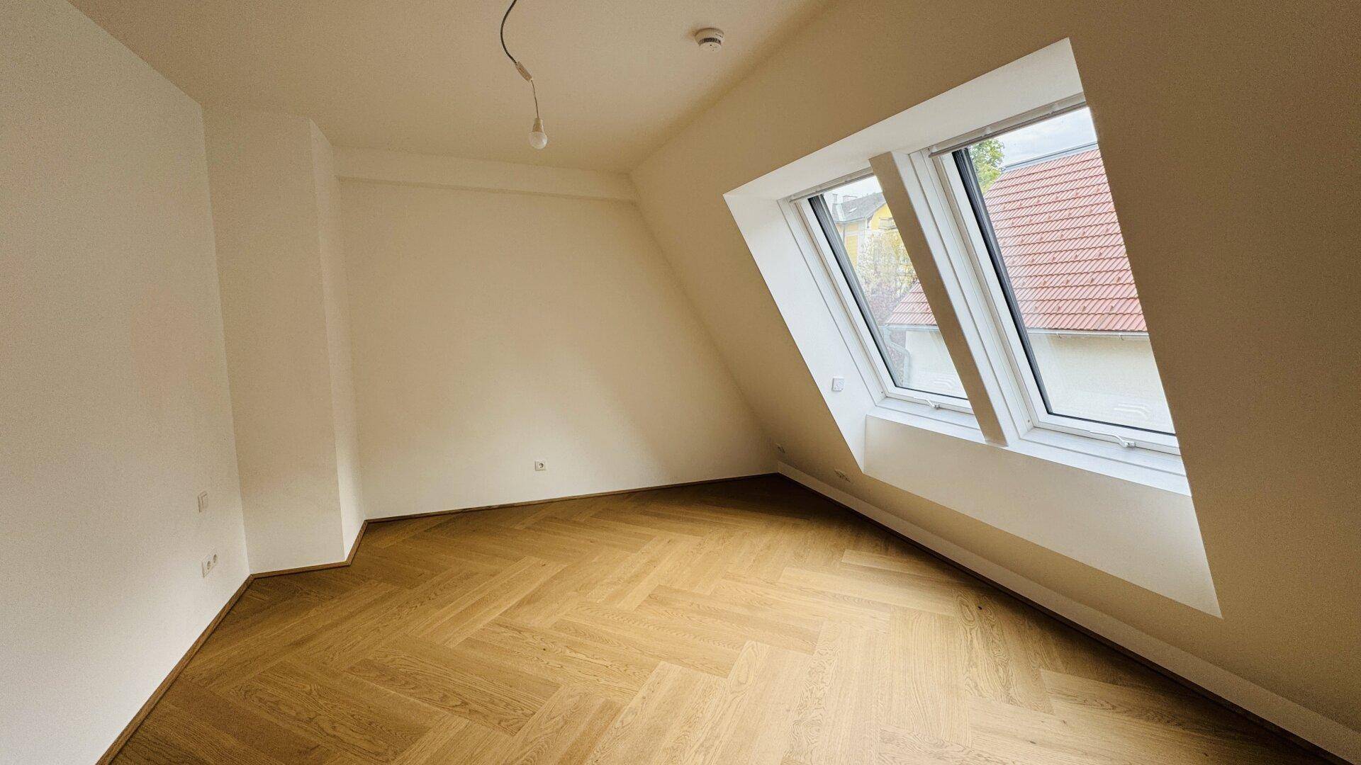 Helles Zimmer im Dachgeschoss mit schrägen Wänden und Dachfenstern.