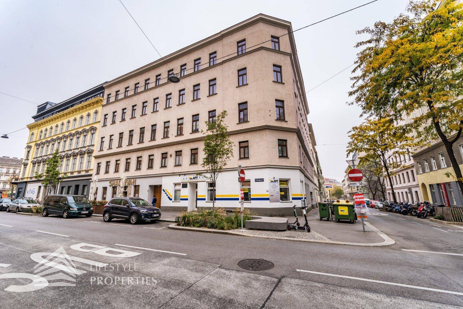 Eckgebäude mit mehreren Etagen und klassischer Architektur, umgeben von einer belebten Stadtstraße.