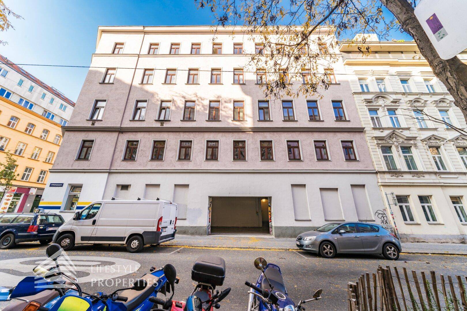 Ansicht der Gebäudefassade von der Straße mit sichtbarer Einfahrt zur Tiefgarage und parkenden Fahrzeugen.