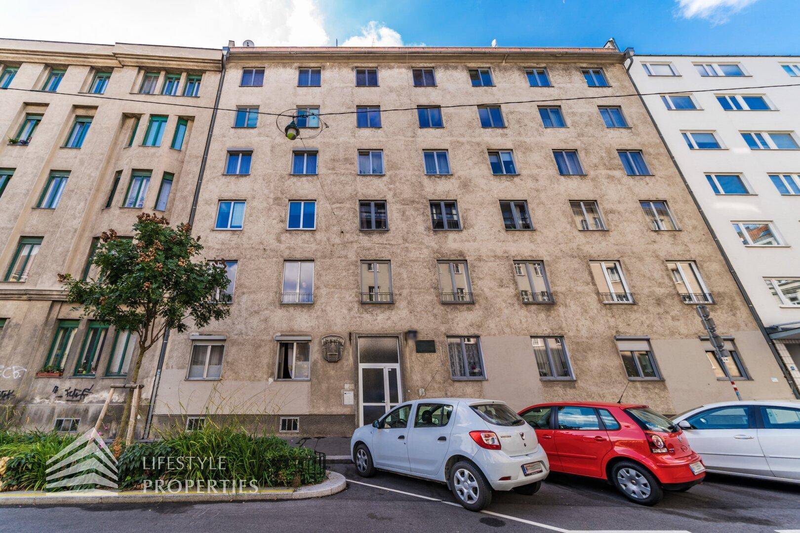 Fassade eines Mehrfamilienhauses mit parkenden Autos davor.