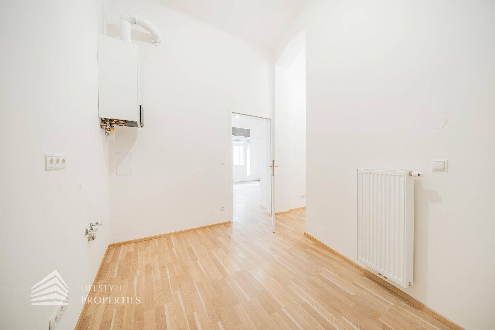 Heller Raum mit Holzboden, Heiztherme und sichtbaren Anschlüssen, ideal als Hauswirtschaftsraum.