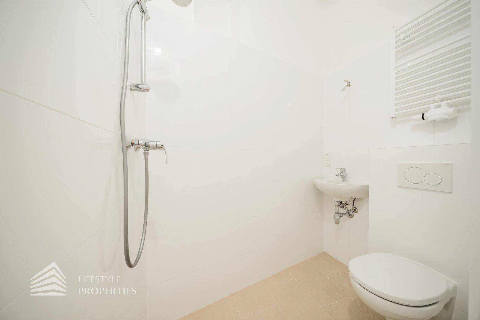 Modernes Badezimmer mit weißen Fliesen, ebenerdiger Dusche und wandhängendem WC.