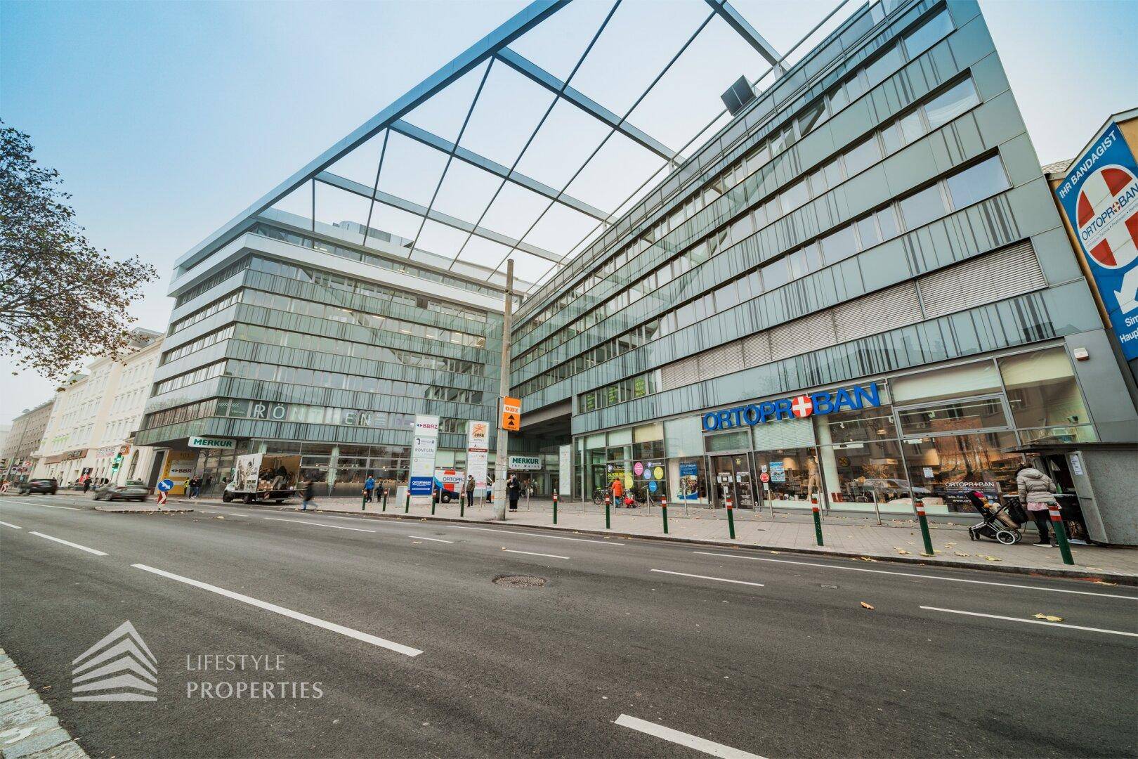 Moderne Geschäftsfassade mit großen Glasflächen und einer markanten Stahlkonstruktion über der Straße.