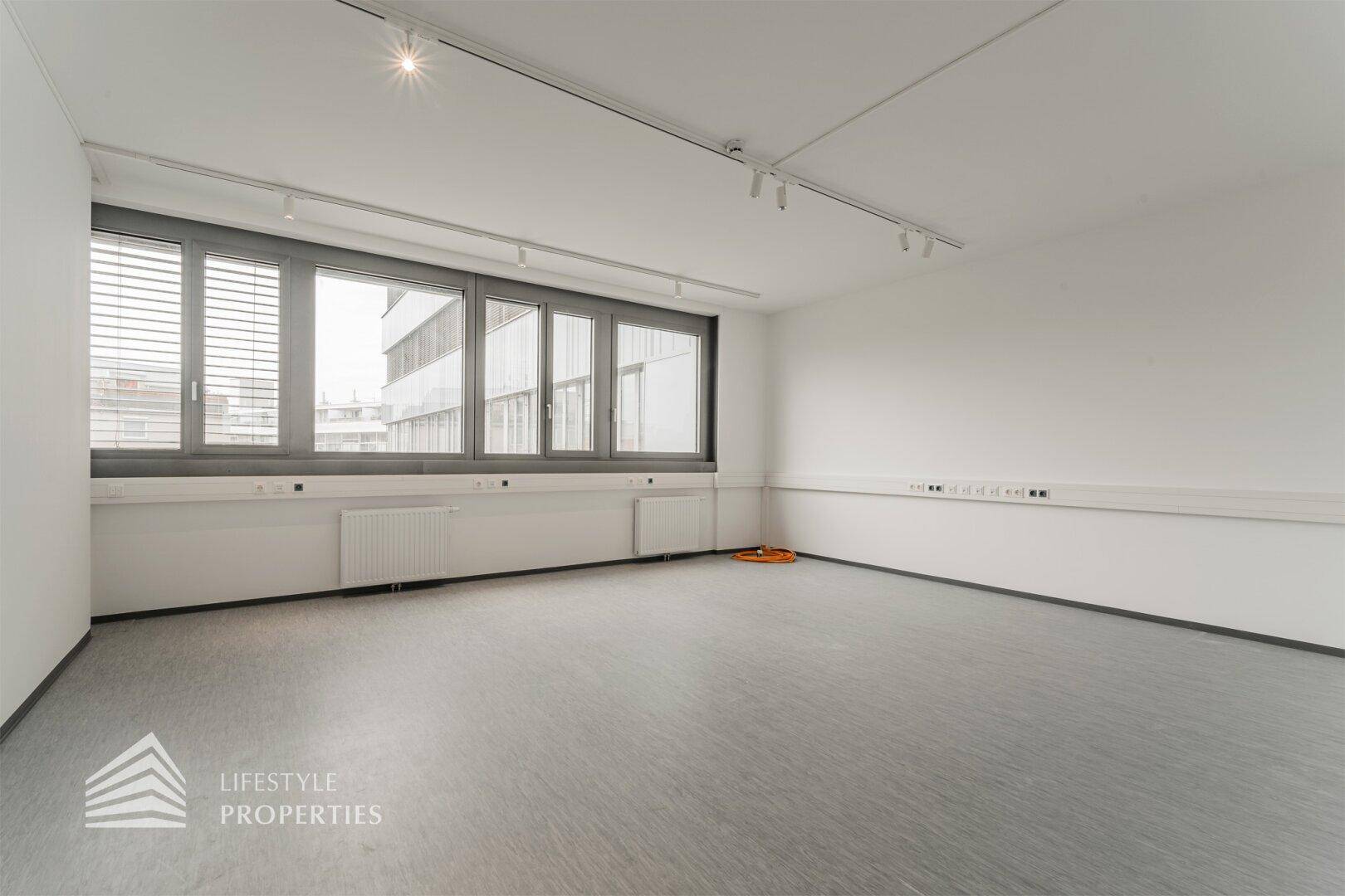 Moderner Büroraum mit großen Fenstern, die einen Blick auf die angrenzenden Gebäude und die Stadt bieten.