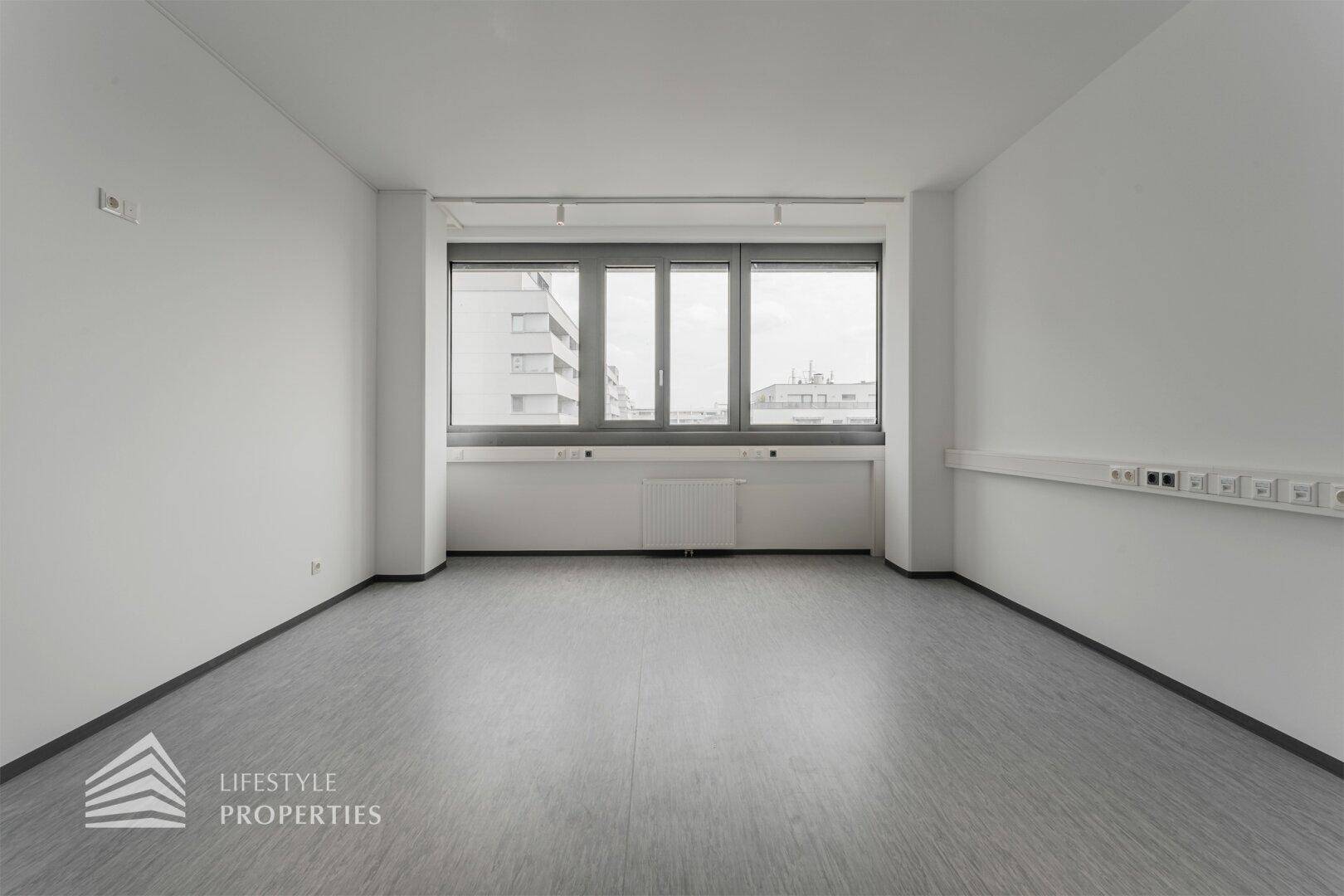 Heller Büroraum mit breiten Fenstern, die einen Panoramablick auf die Stadtlandschaft ermöglichen und den Raum erhellen.