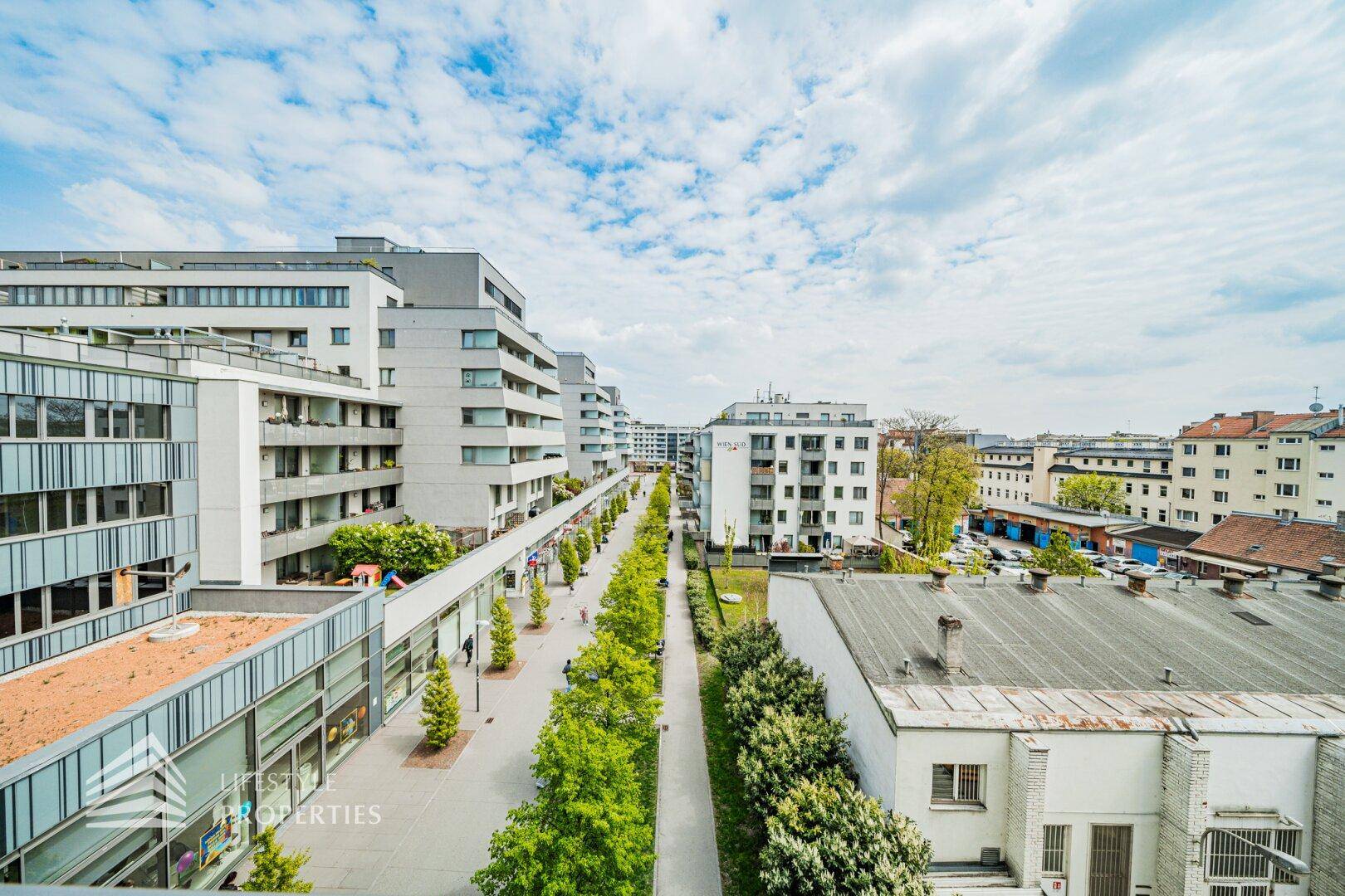 Weitläufige Ansicht eines modernen Wohnkomplexes mit begrünten Wegen und zahlreichen Balkonen unter blauem Himmel.