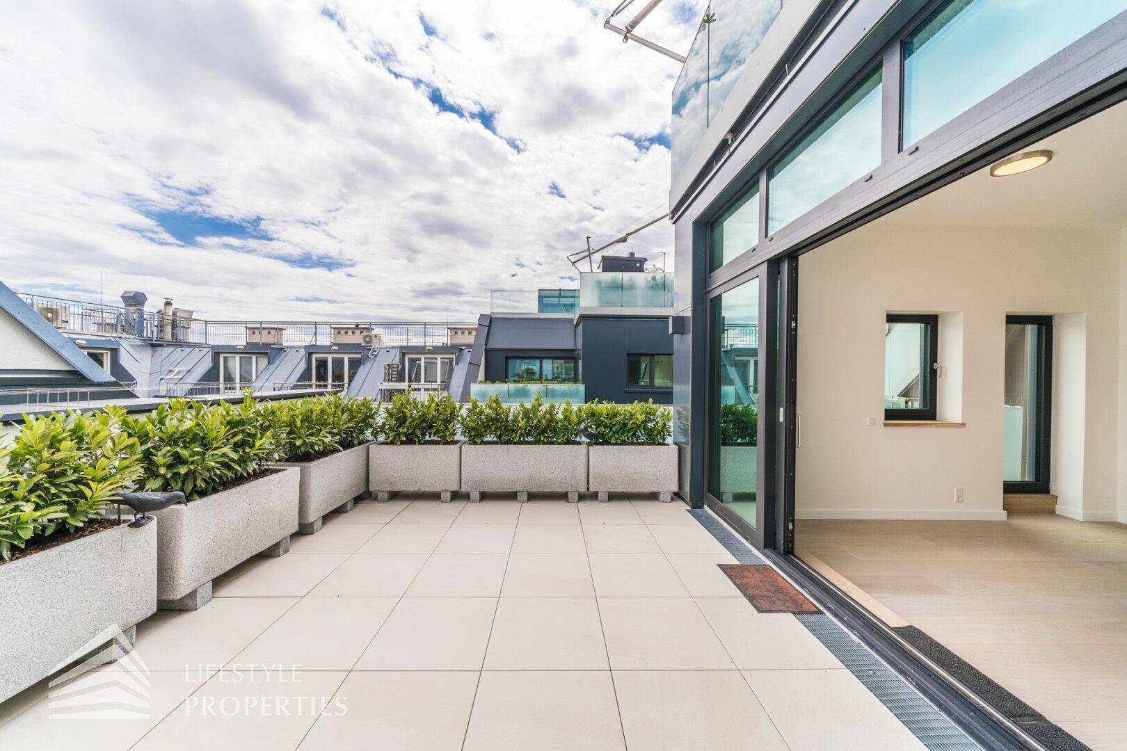 Geräumige Dachterrasse mit großen Schiebetüren, Pflanzenkübeln und Blick auf die Dächer der Stadt.