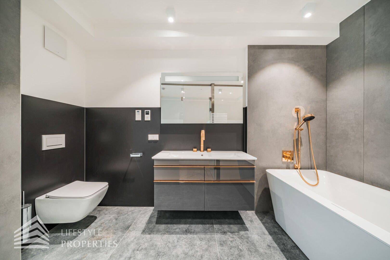 Stilvolles Badezimmer mit Wand-WC, Einzelwaschbecken und freistehender Badewanne in Grau und Weiß.