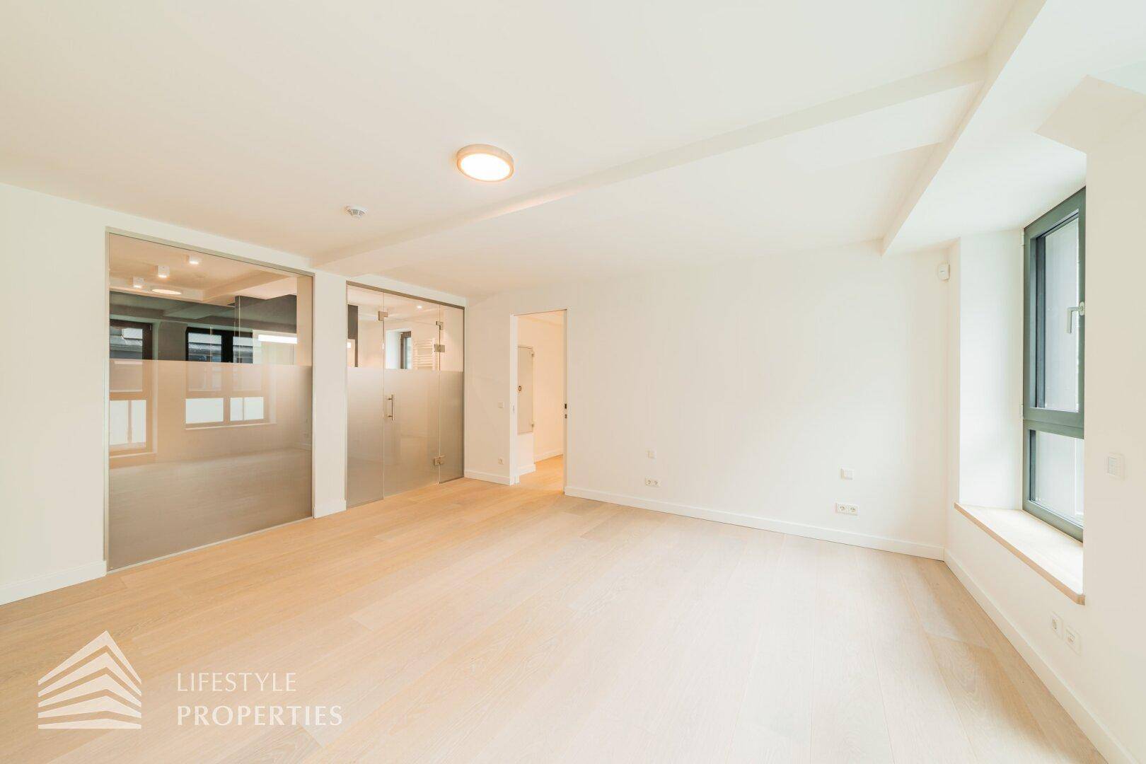 Geräumiger, heller Raum mit Holzboden und großen Fenstern, ideal für verschiedene Nutzungsmöglichkeiten.