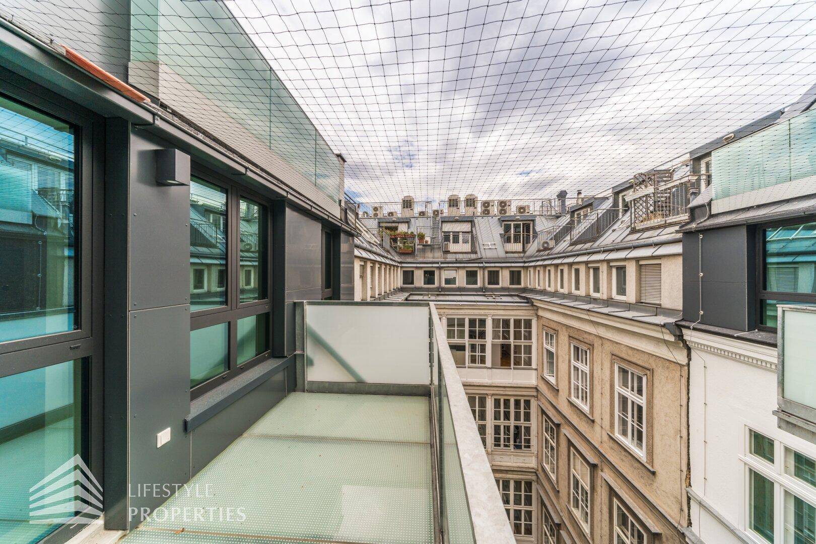 Moderner Balkon mit Blick auf einen historischen Innenhof und umliegende Gebäude.