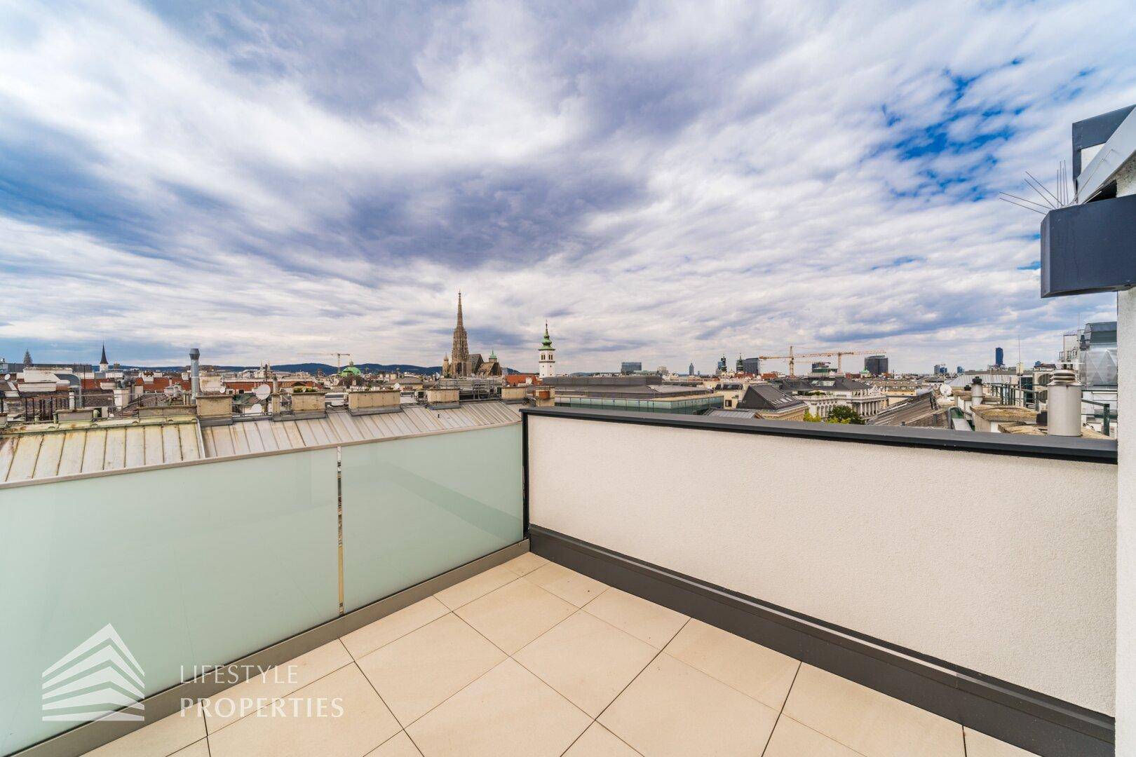 Dachterrasse mit Panoramablick über die Stadt und ihre historischen Wahrzeichen unter bewölktem Himmel.