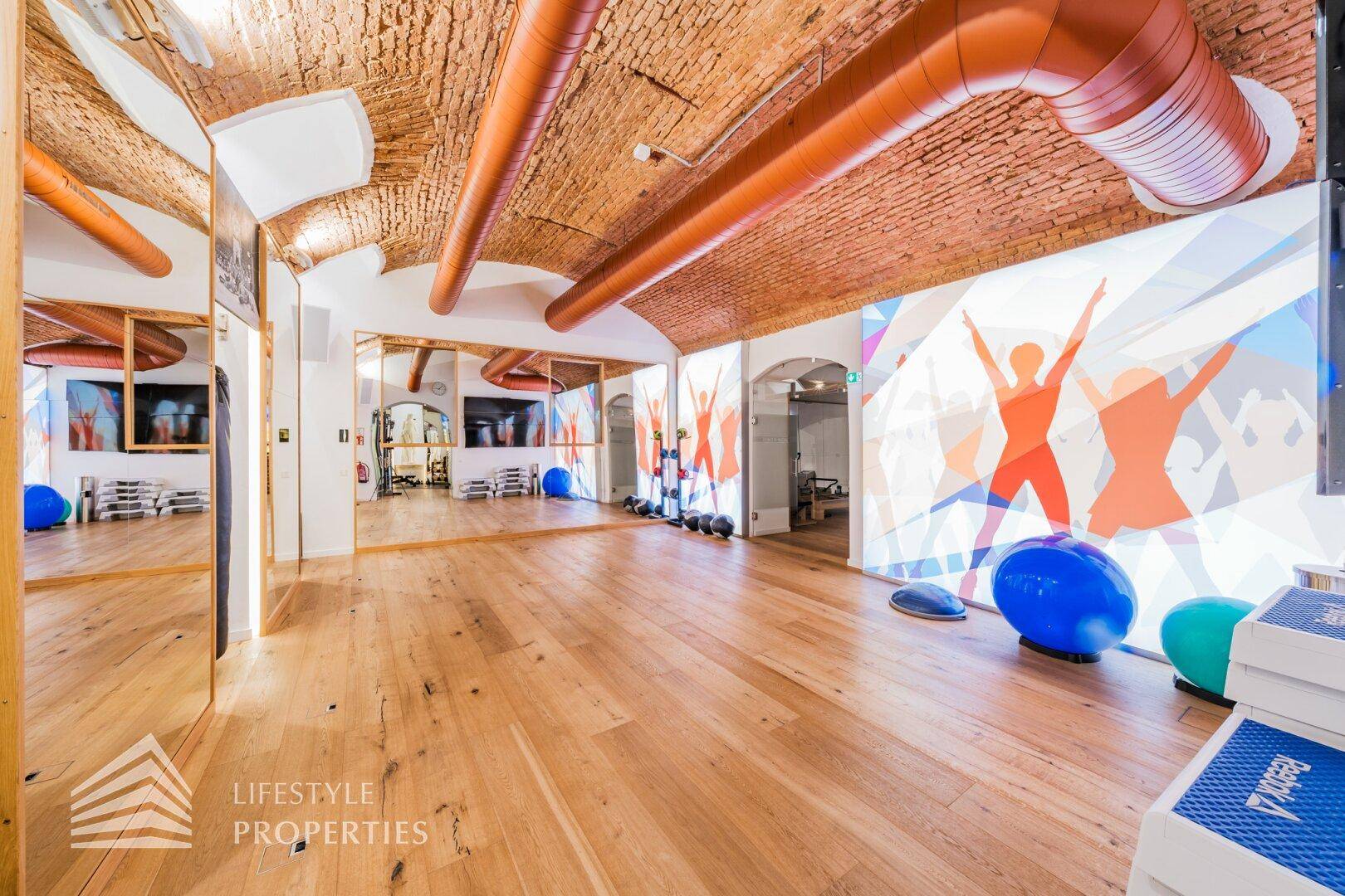 Vielseitiger Trainingsraum mit Spiegelwänden, Gymnastikbällen und interaktiver Projektion an der Wand.
