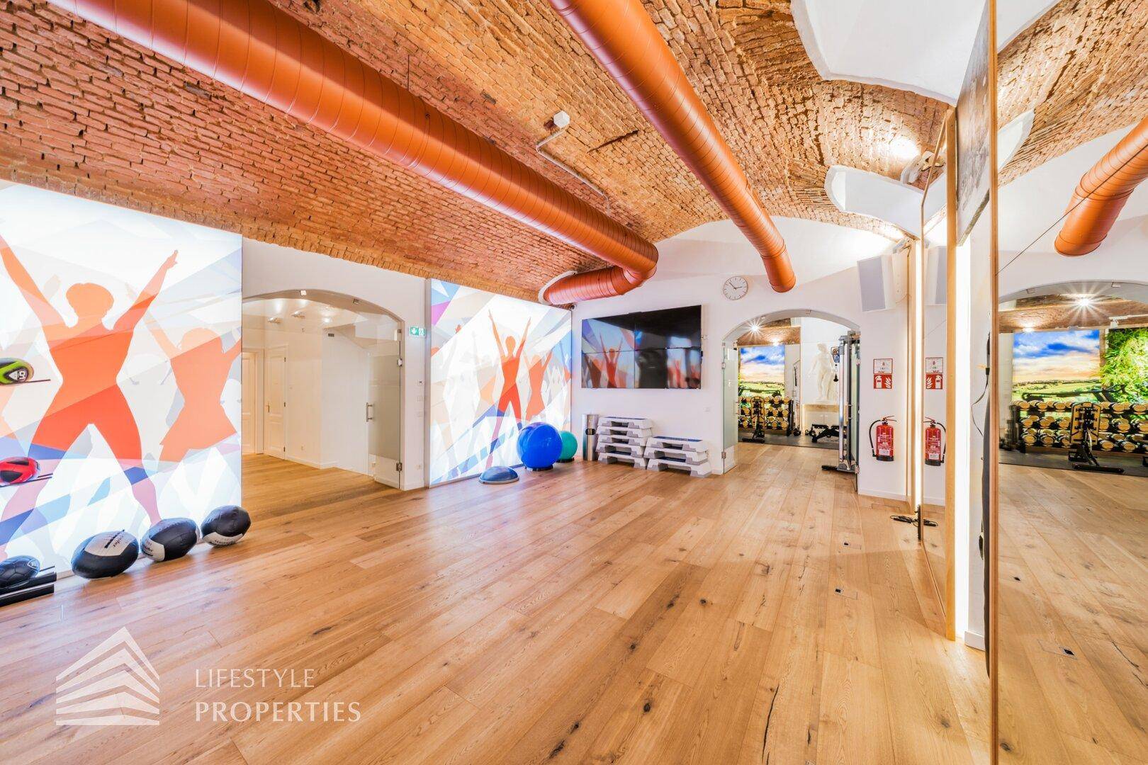 Heller Trainingsraum mit Holzboden, großen Spiegeln und moderner Wandprojektion für verschiedene Kurse.