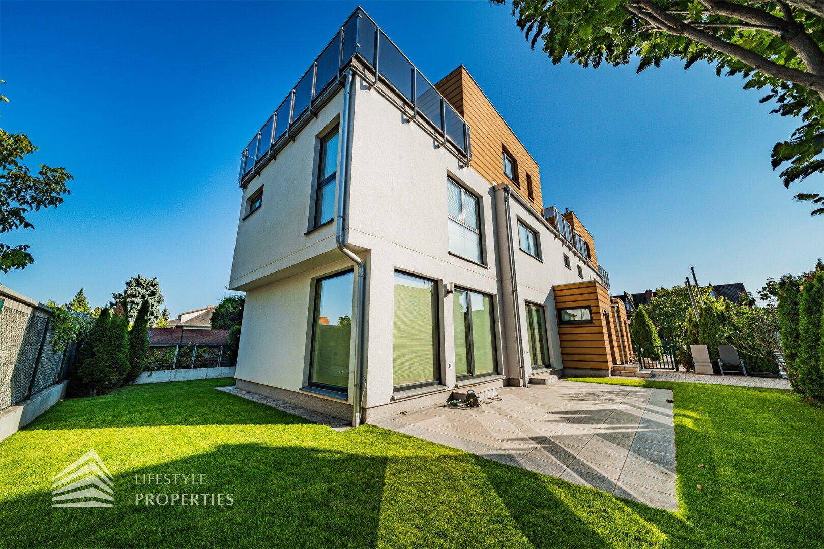 Moderne Hausfassade mit großen Fenstern, umgeben von einem gepflegten Rasen und einer Terrasse.