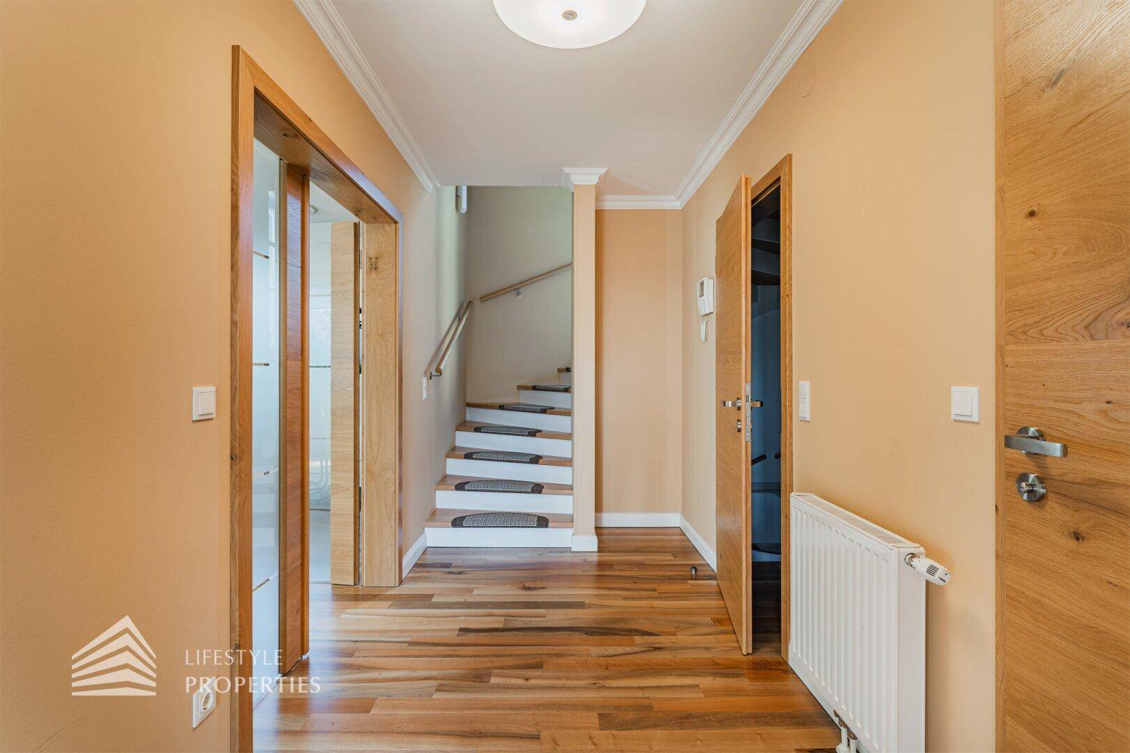 Heller Flur mit Holzfußboden und Zugang zu einer Treppe, die in die oberen Etagen führt.