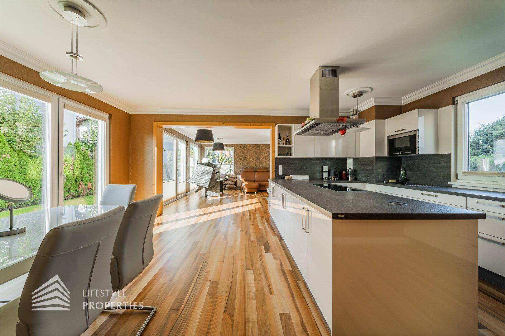 Moderne offene Küche mit weißer Hochglanzfront, Kücheninsel und Essbereich, verbunden mit dem Wohnzimmer.