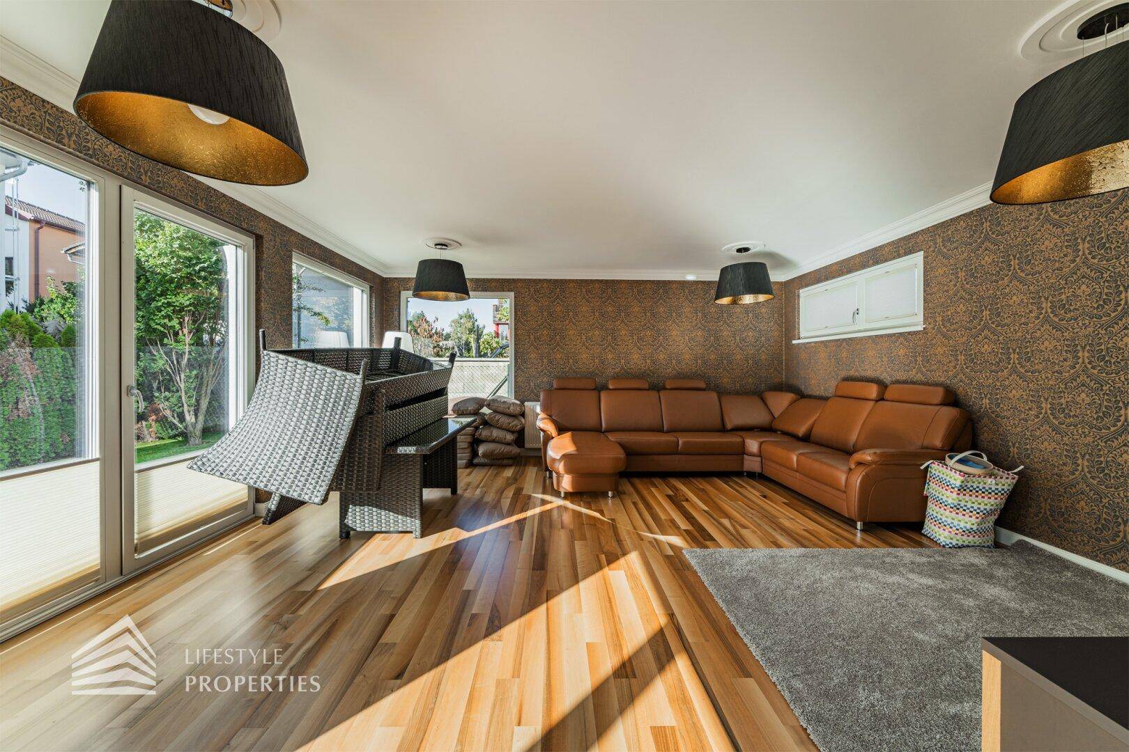 Gemütliches Wohnzimmer mit großem Ecksofa, Holzboden und Zugang zu einer Terrasse mit Gartenblick.
