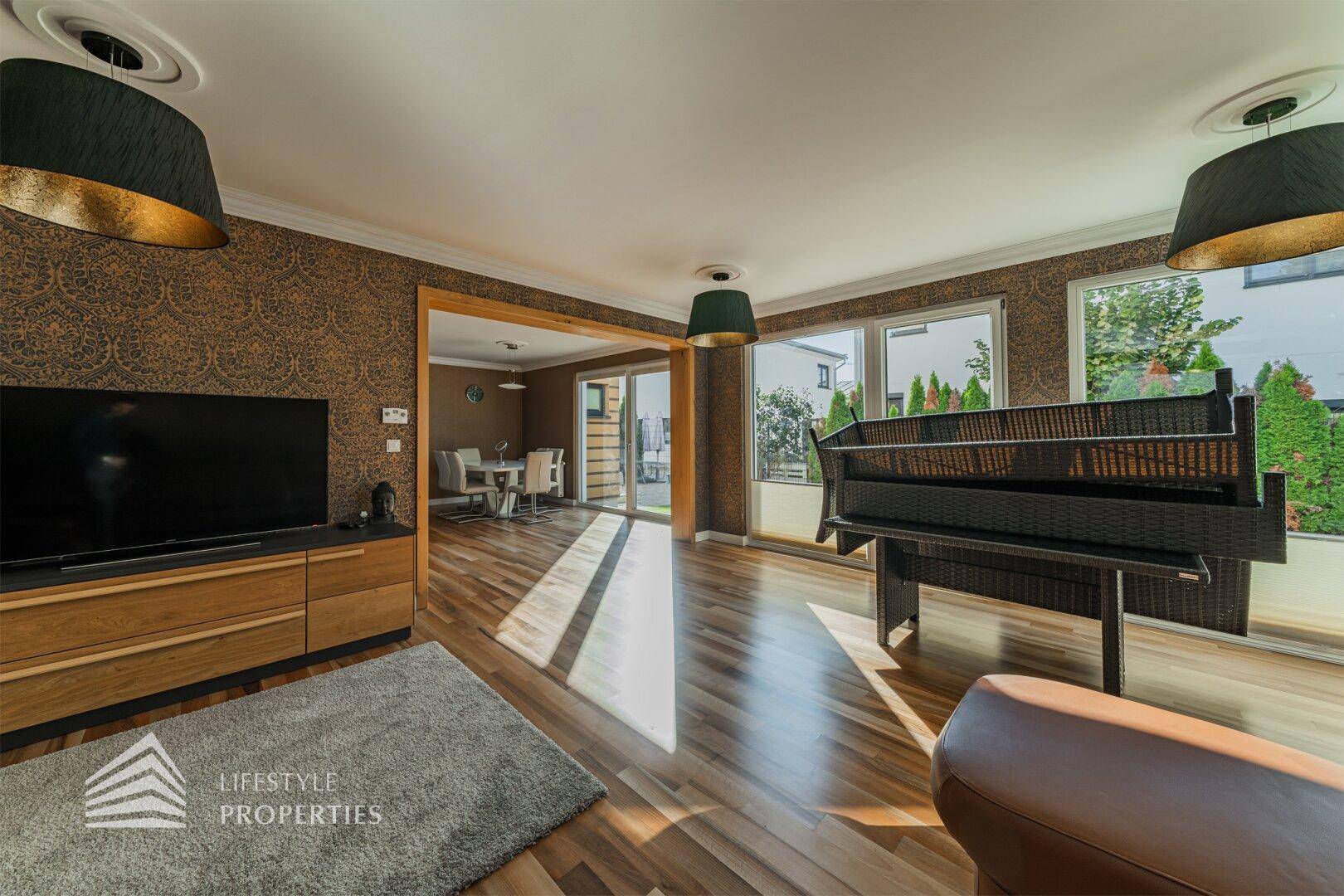 Helles Wohnzimmer mit Holzboden, TV-Möbel und Blick in den angrenzenden Essbereich und die Küche.