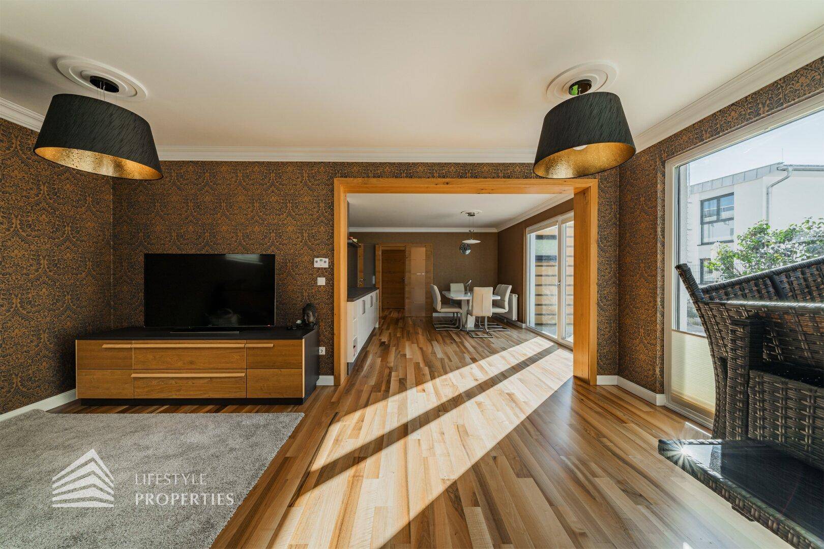 Geräumiges Wohnzimmer mit Holzboden, großen Fenstern und offener Verbindung zum Ess- und Küchenbereich.