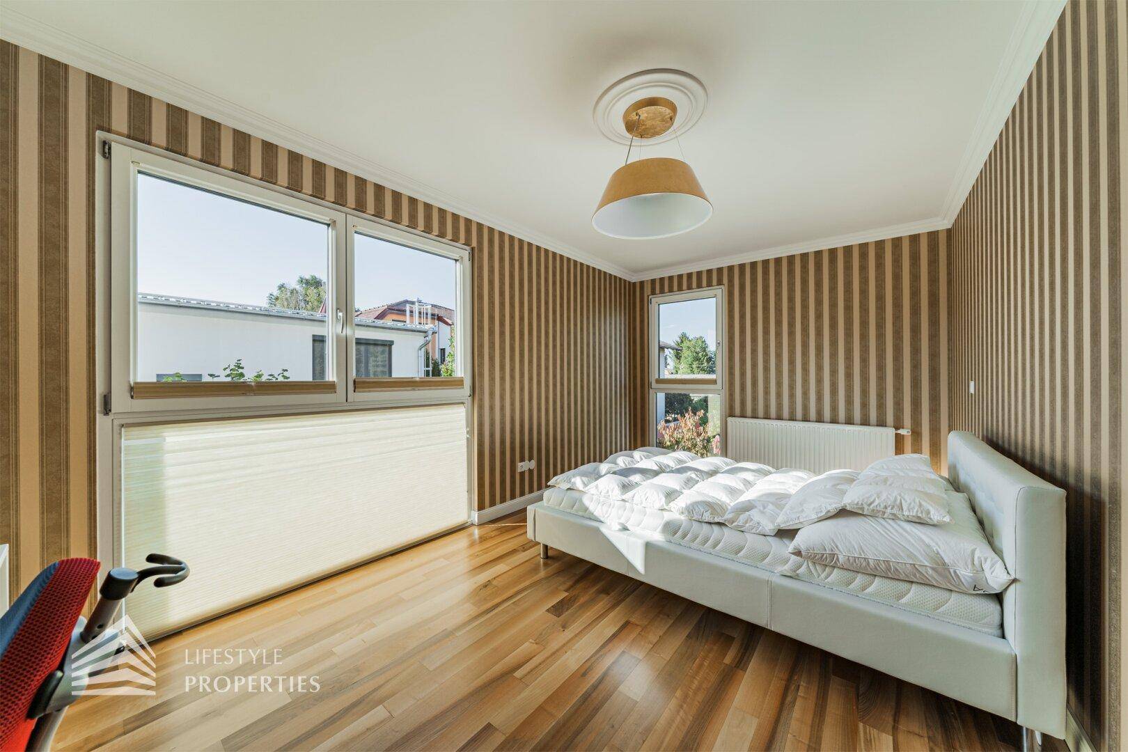 Helles Schlafzimmer mit gestreifter Tapete, Holzboden und großen Fenstern für viel Tageslicht.