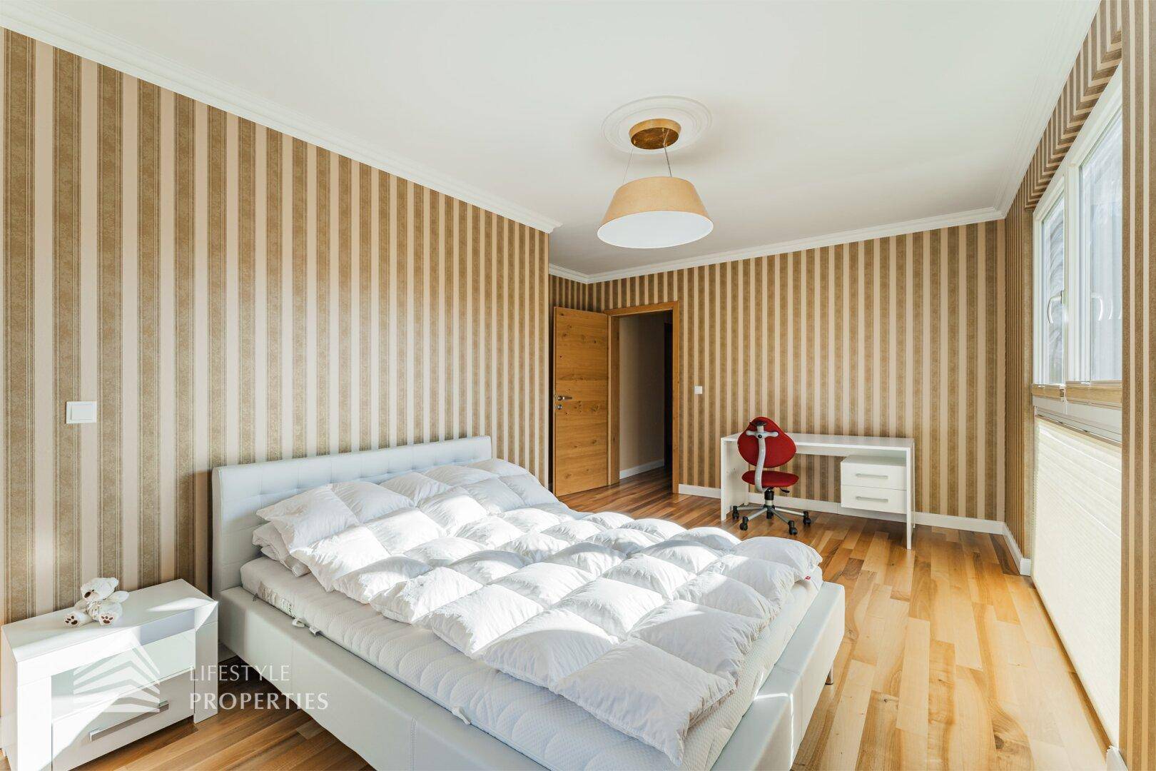 Gemütliches Schlafzimmer mit Holzboden, gestreifter Tapete und einem kleinen Schreibtischbereich.