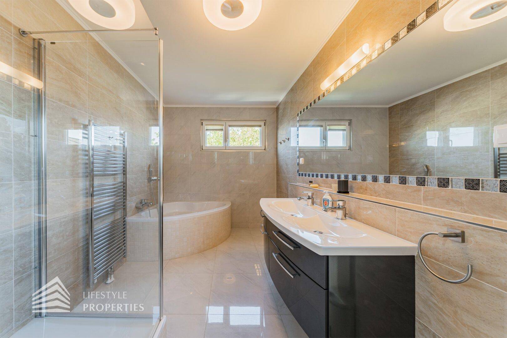 Modernes Badezimmer mit Doppelwaschbecken, Duschkabine, Eckbadewanne und beheiztem Handtuchhalter.