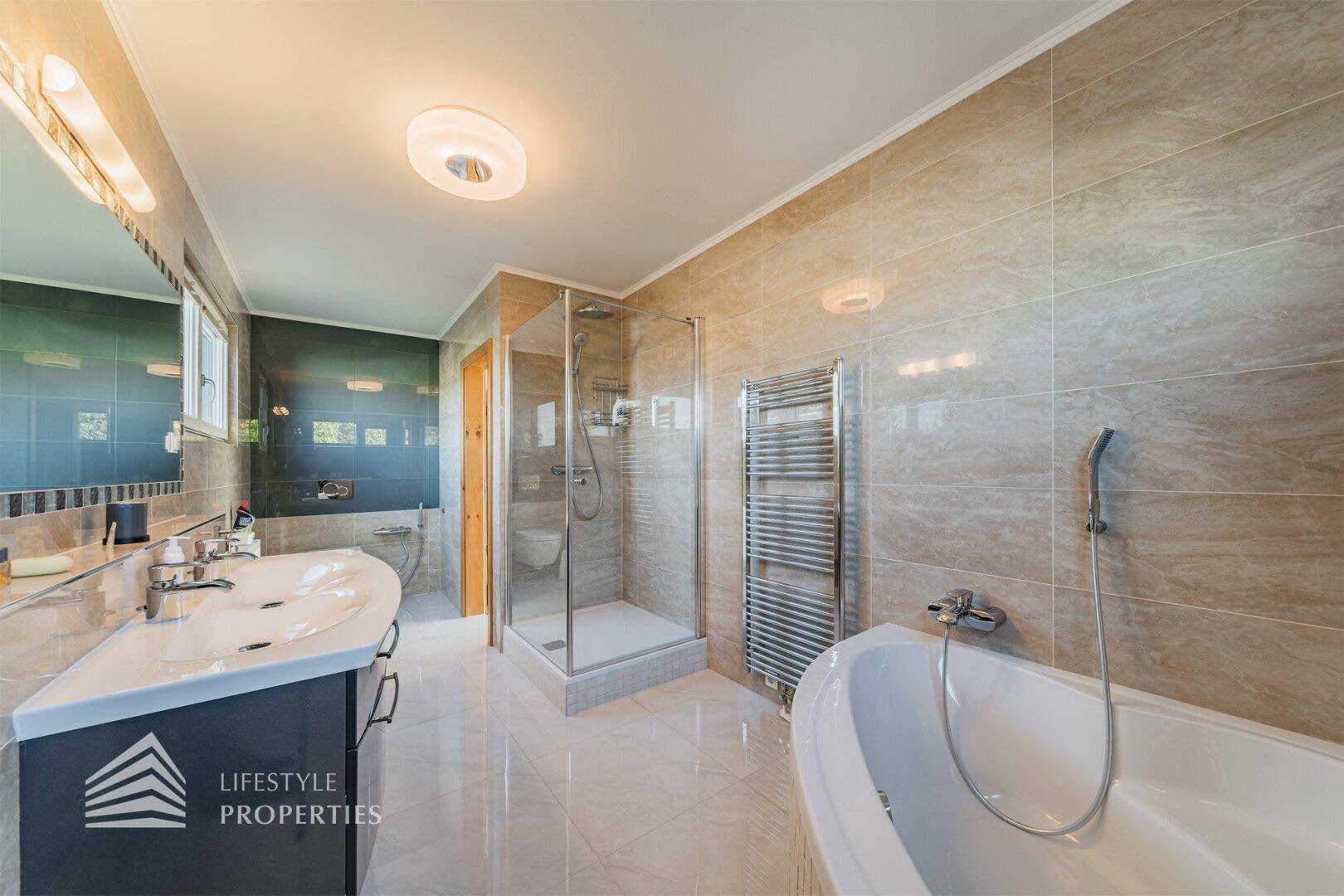 Geräumiges Badezimmer mit Doppelwaschbecken, Duschkabine, Eckbadewanne und hellen Fliesen.