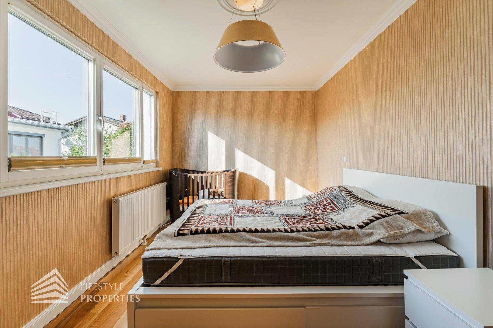 Helles Schlafzimmer mit gemusterter Tapete, Holzboden und einem Fenster, das viel Licht spendet.