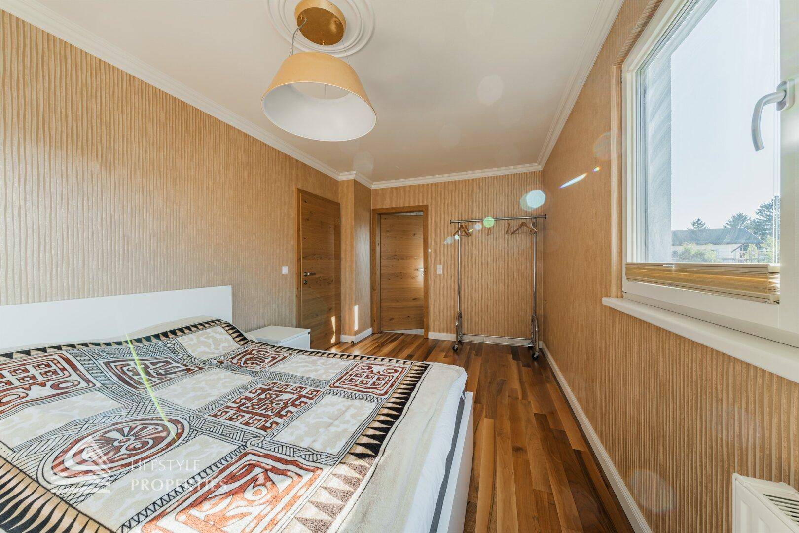 Gemütliches Schlafzimmer mit Holzboden, gemusterter Tapete und einem praktischen Kleiderständer.
