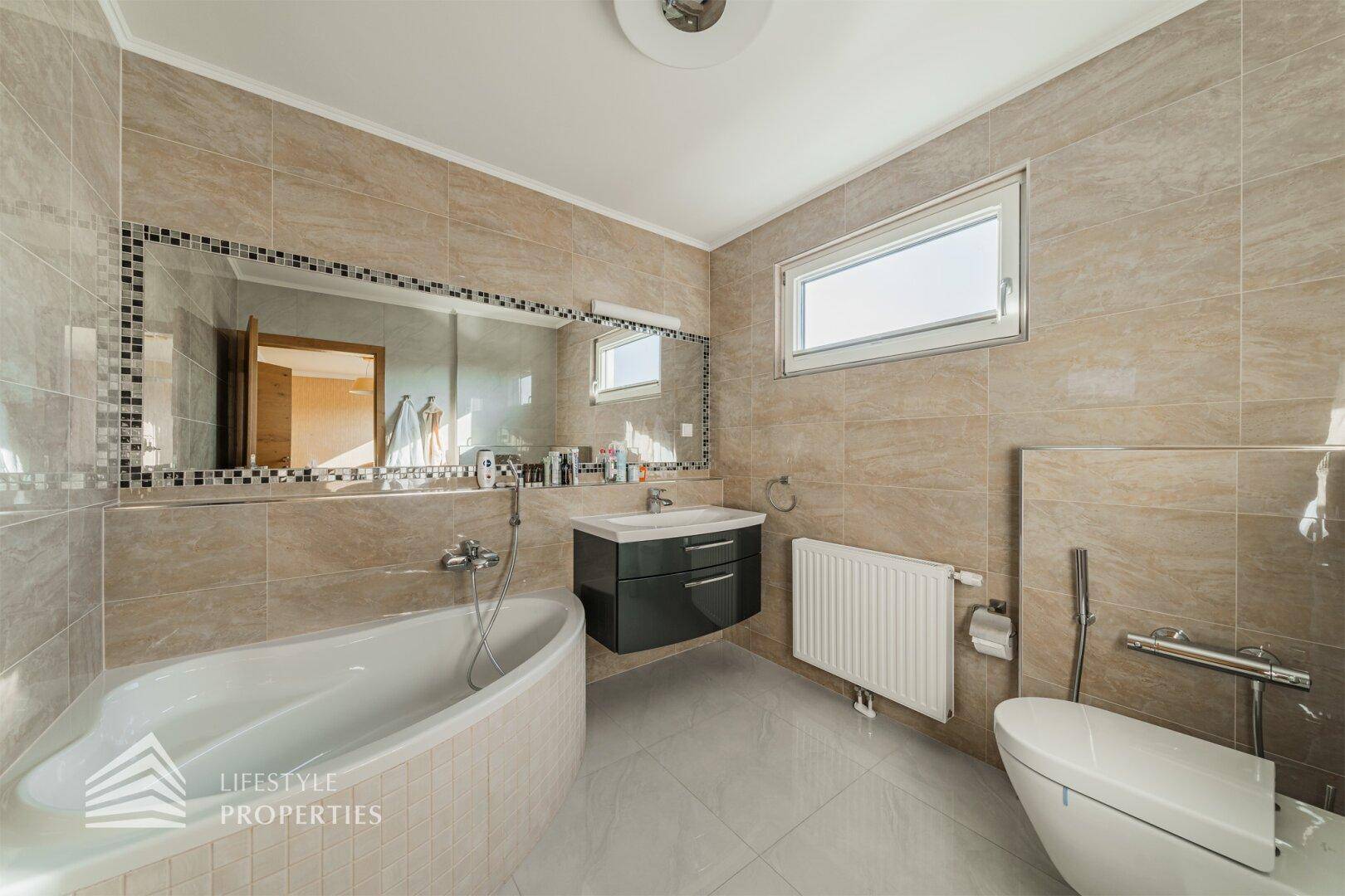 Modernes Badezimmer mit Badewanne, Wandwaschbecken, Wand-WC und hellen Fliesen an Wänden und Boden.