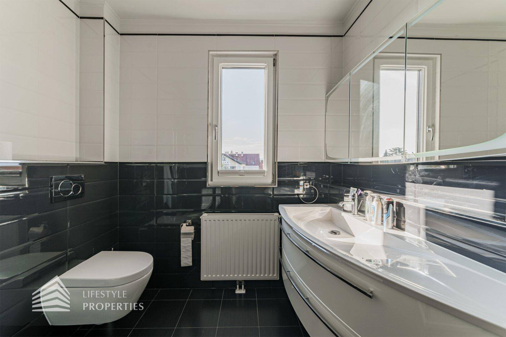 Modernes Badezimmer in Schwarz-Weiß mit Waschbecken, Wand-WC, Duschkabine und Fenster.