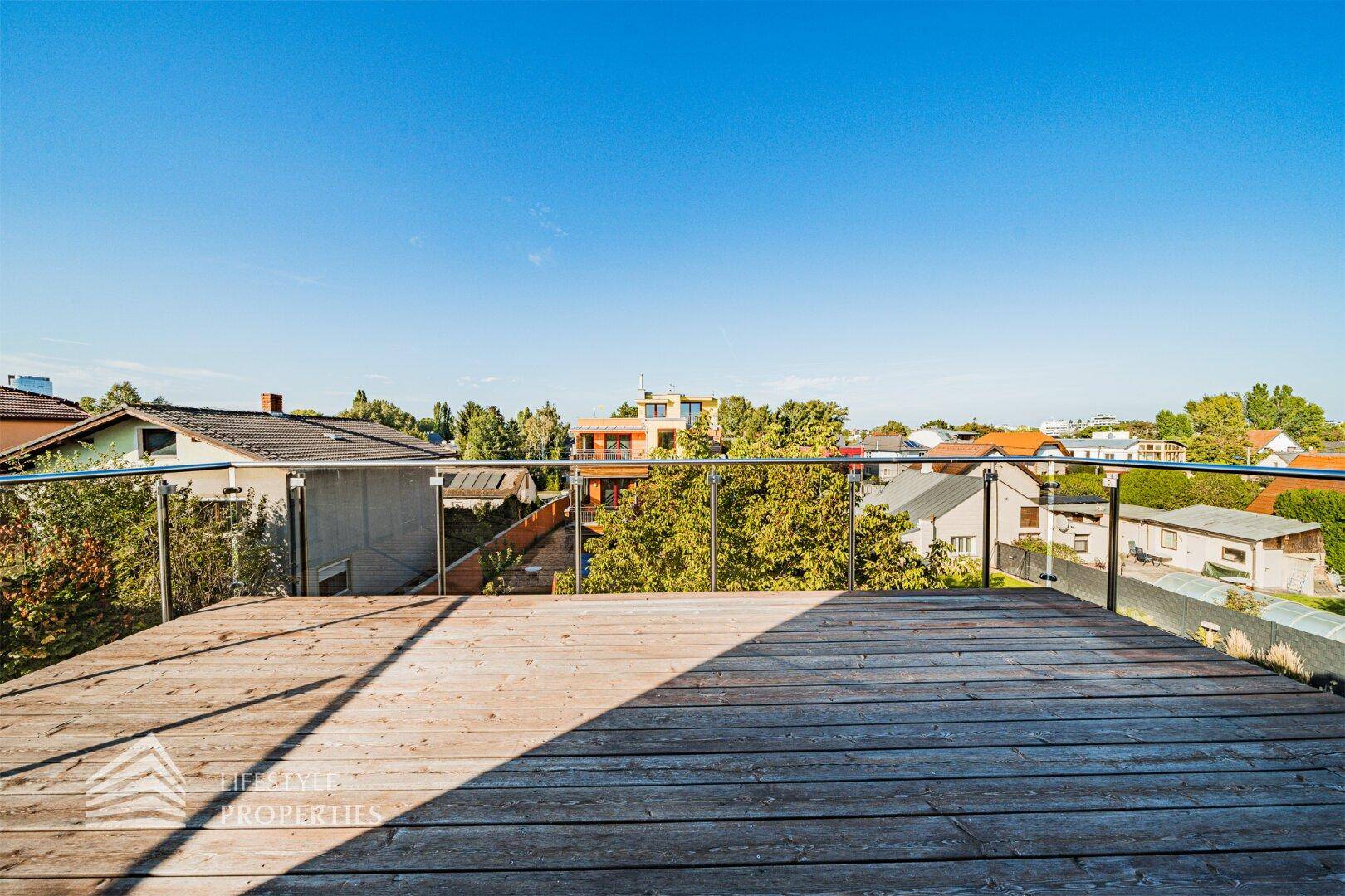 Große Holzterrasse mit Glasgeländer und weitem Blick über die umliegende Nachbarschaft.