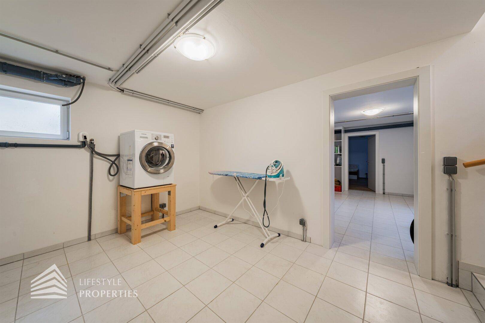 Praktischer Hauswirtschaftsraum im Keller mit Waschmaschine, Bügelbrett und Fliesenboden.